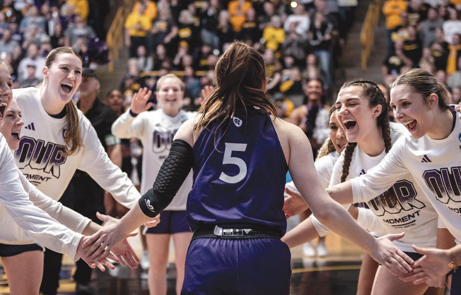 Women basketball players welcome teammate onto court.