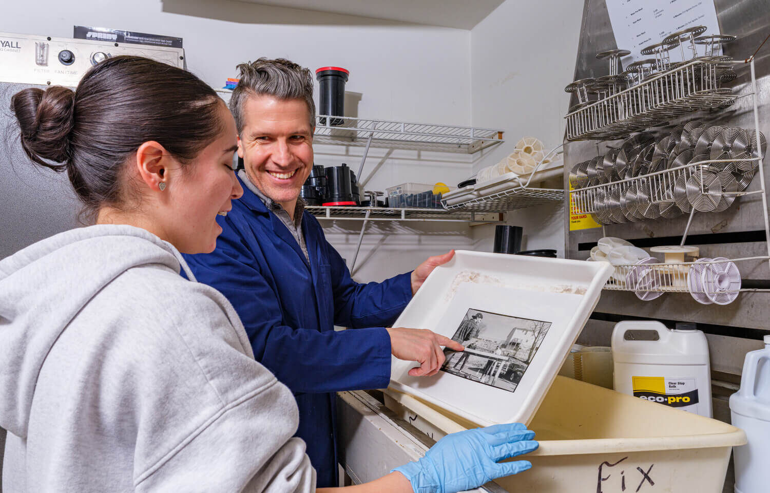 Man and woman look at print developing in a darkroom