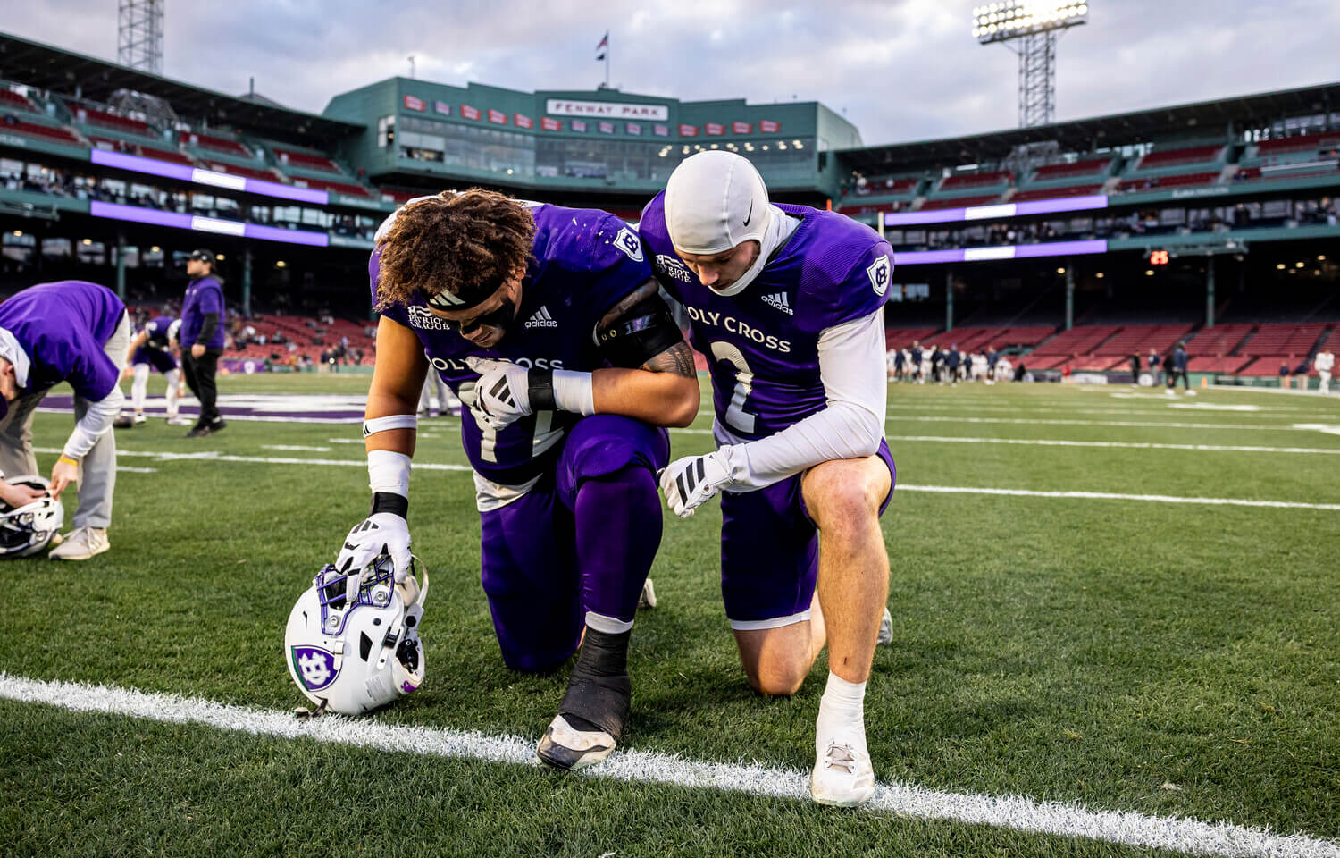 Two Holy Cross football players kneeling on the field