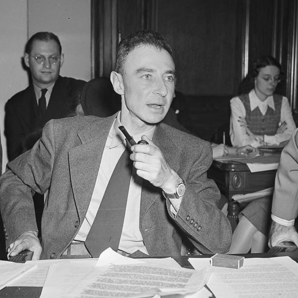 A man at a suit sits at a desk with paperwork covering it