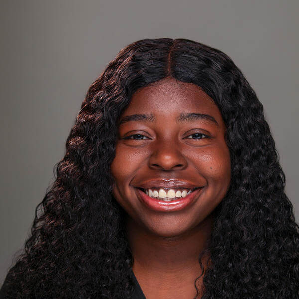 A portrait of a young woman with hair down to her shoulders and a collared shirt smiling