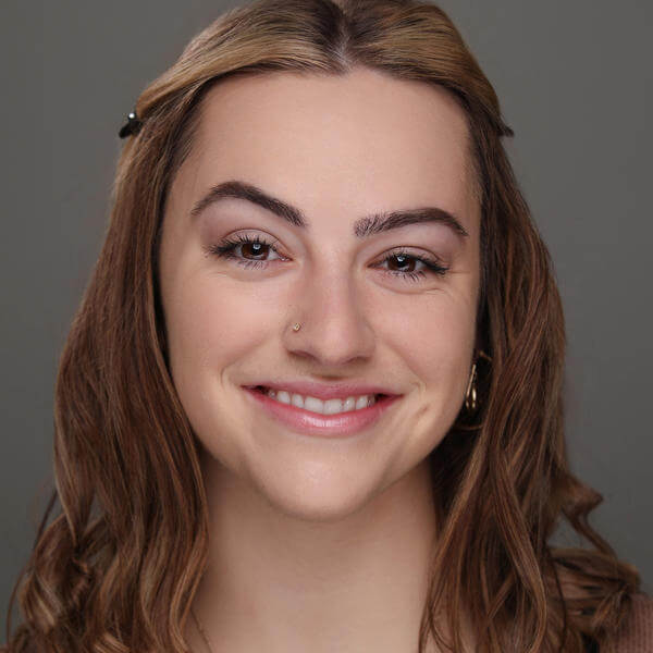 A portrait of a smiling young woman with wavy hair and wearing a gold pendant