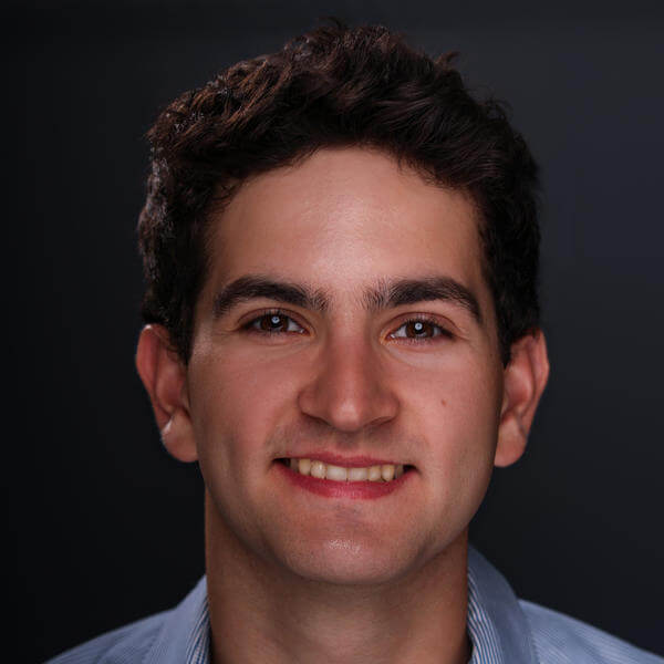 A portrait of a young man smiling with short hair and a collared shirt
