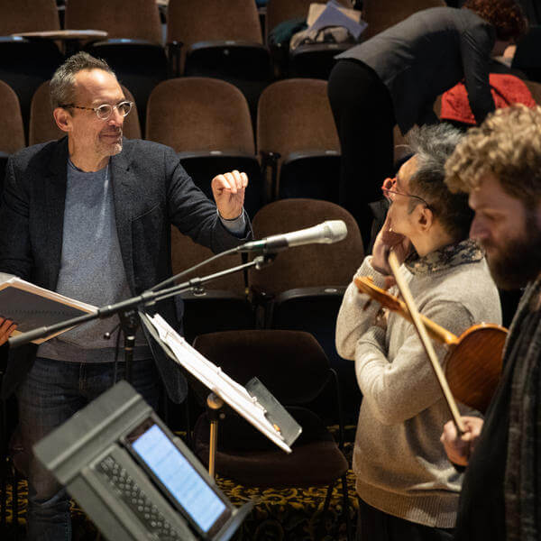 Composer talks with members of an orchestra during rehearsal.