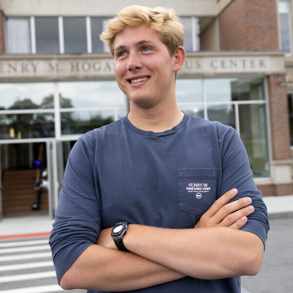 Blonde man standing in front of building with arms crossed.