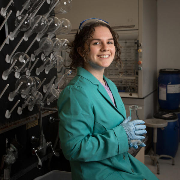 Young woman posing for picture in chemistry lab holding a glass beaker.