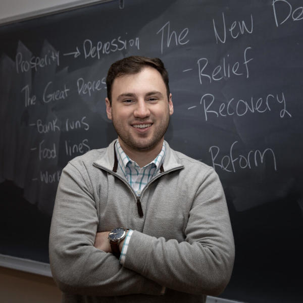 Male college student standing in front of a chalk board.