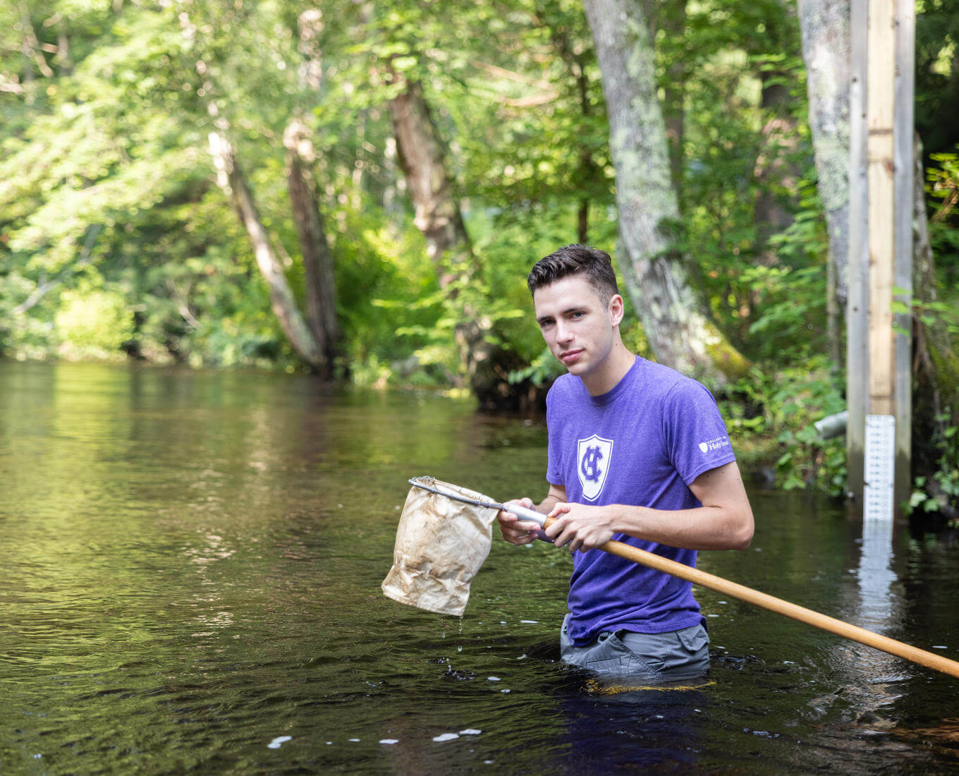 A male student catches insects in the Blackstone River.