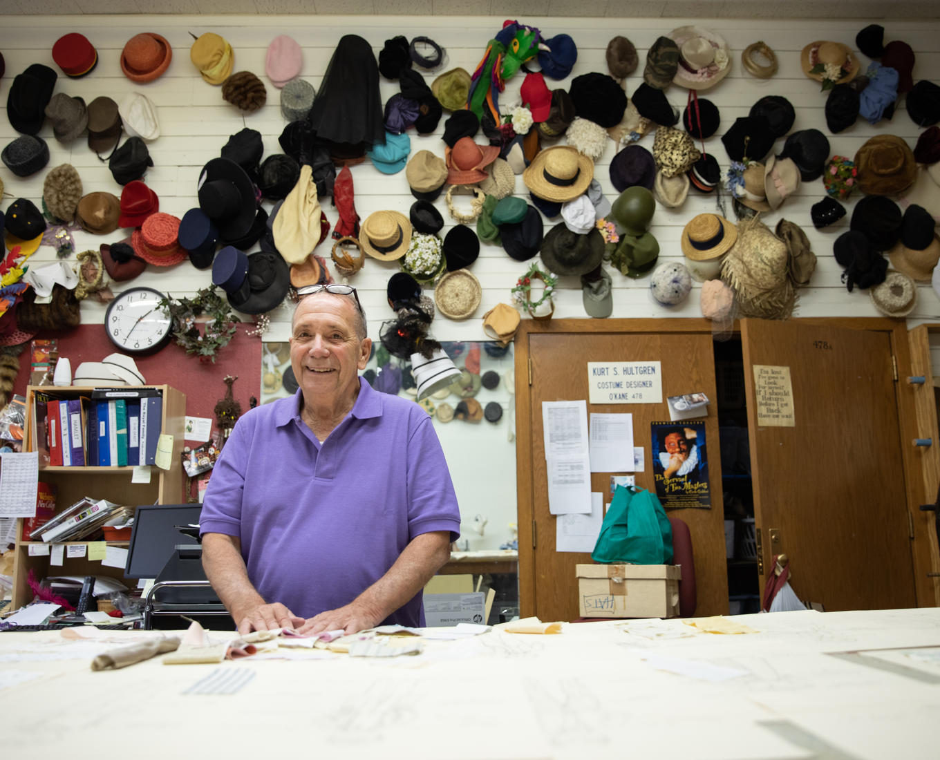 Kurt Hultgren stands in his costume shop in front of a wall full of hats.