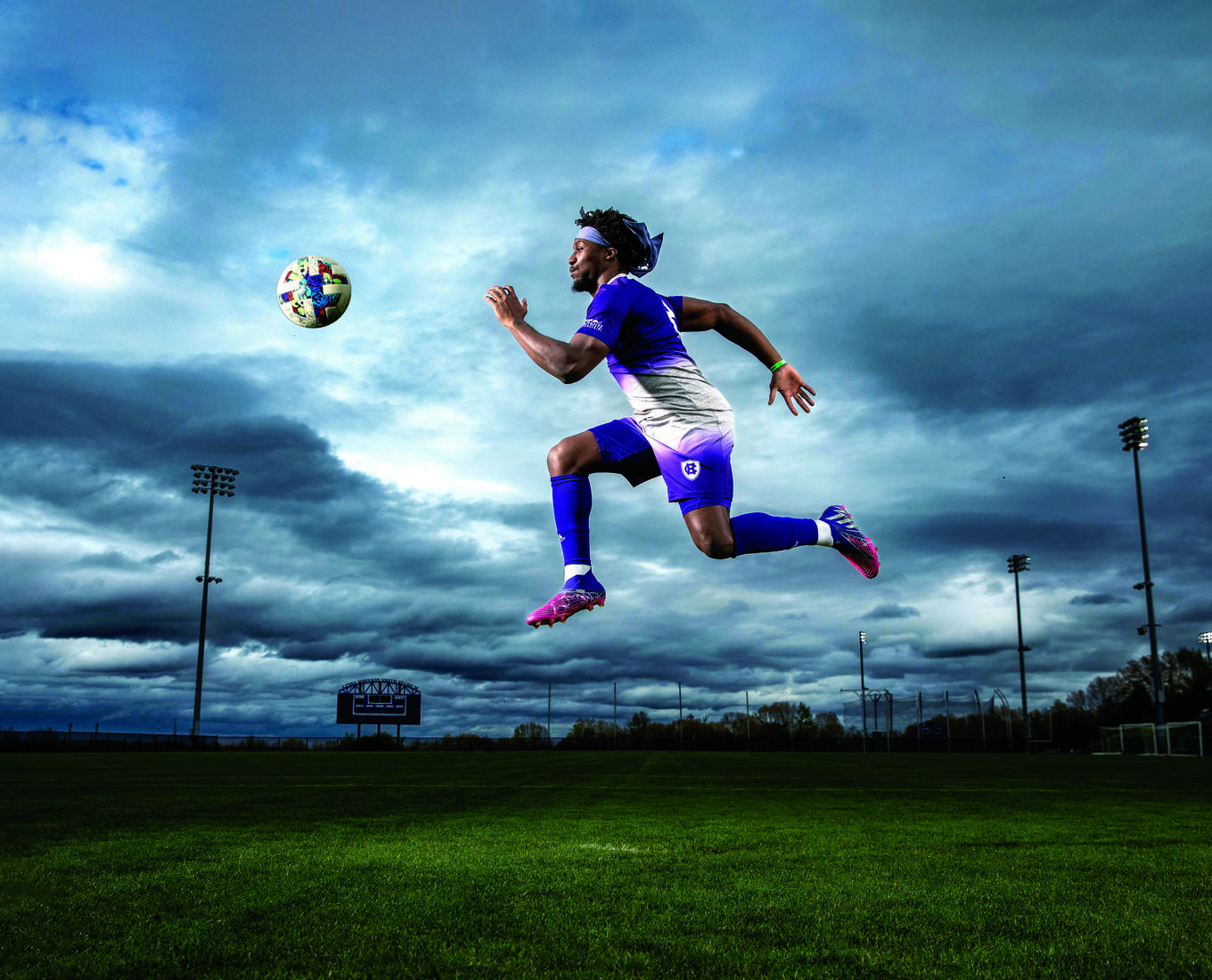 A soccer player in a purple uniform jumping in the air for a soccer ball that is at eye level