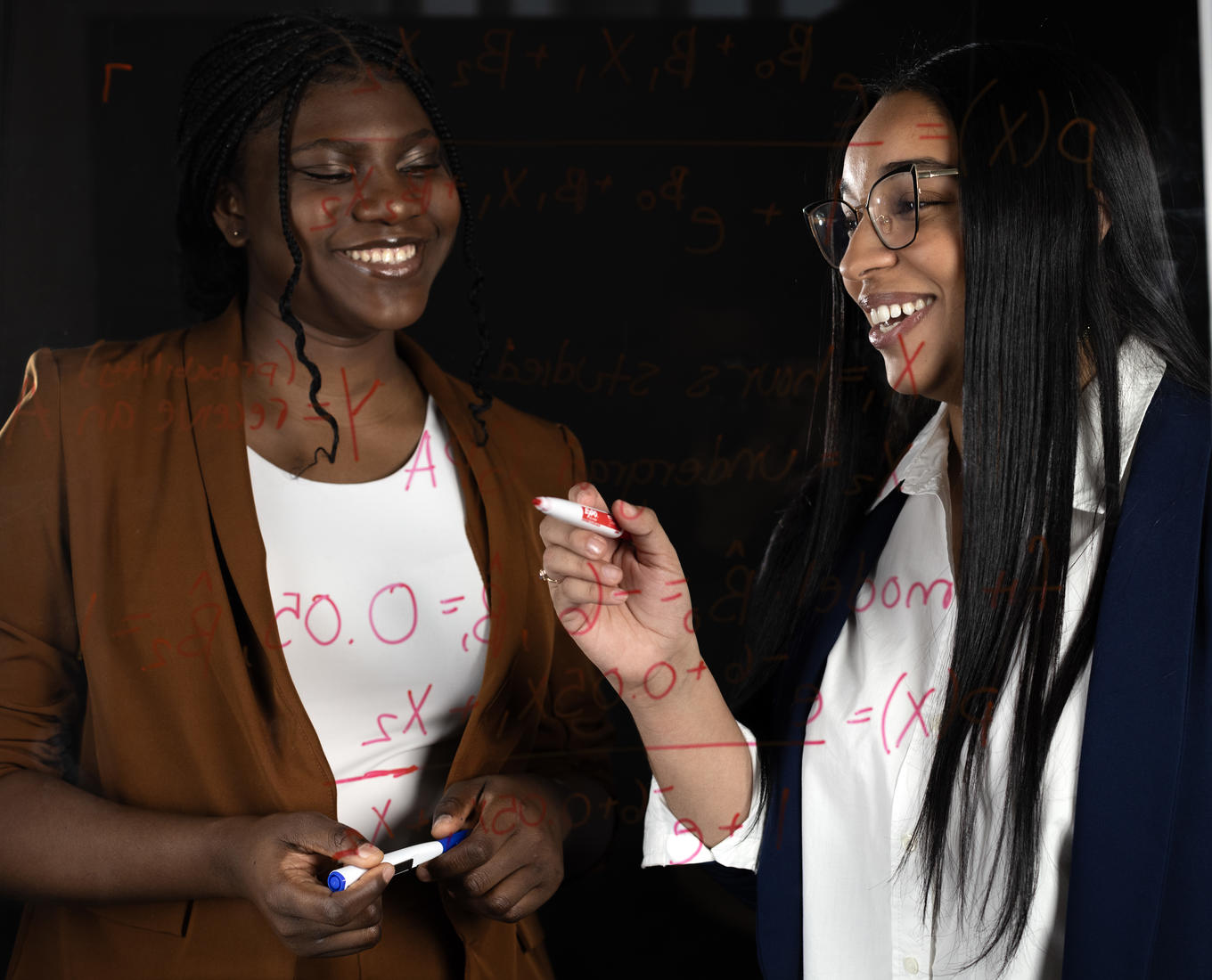 Two women write equations on a window. 