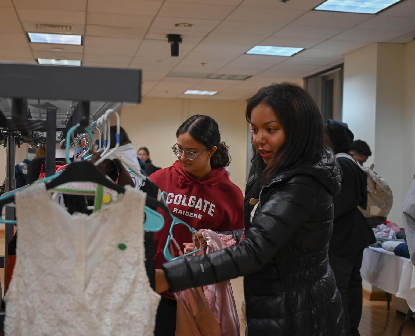 Young women look through thrift store clothing racks.