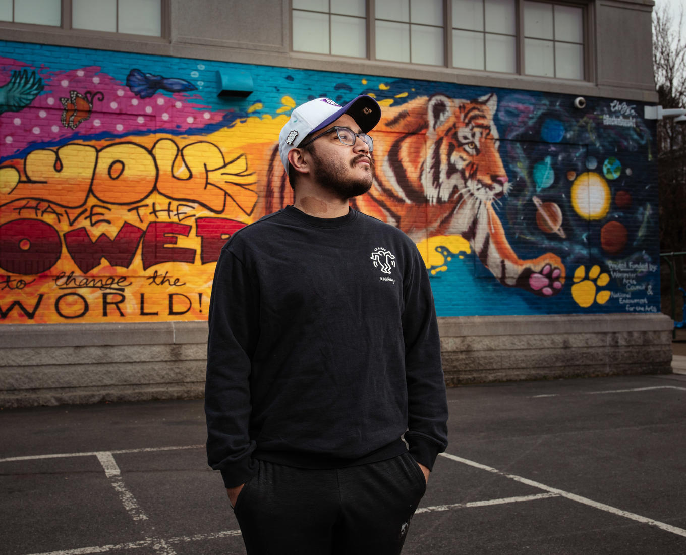 Man in hat stands in front of mural