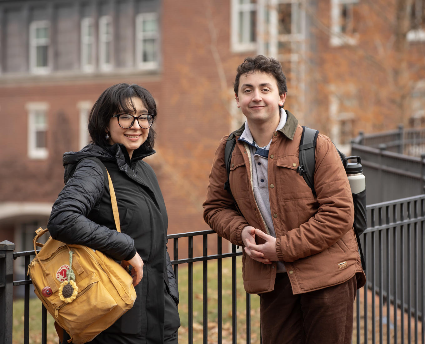 A female and a male student pose for a picture in front of a brick building.