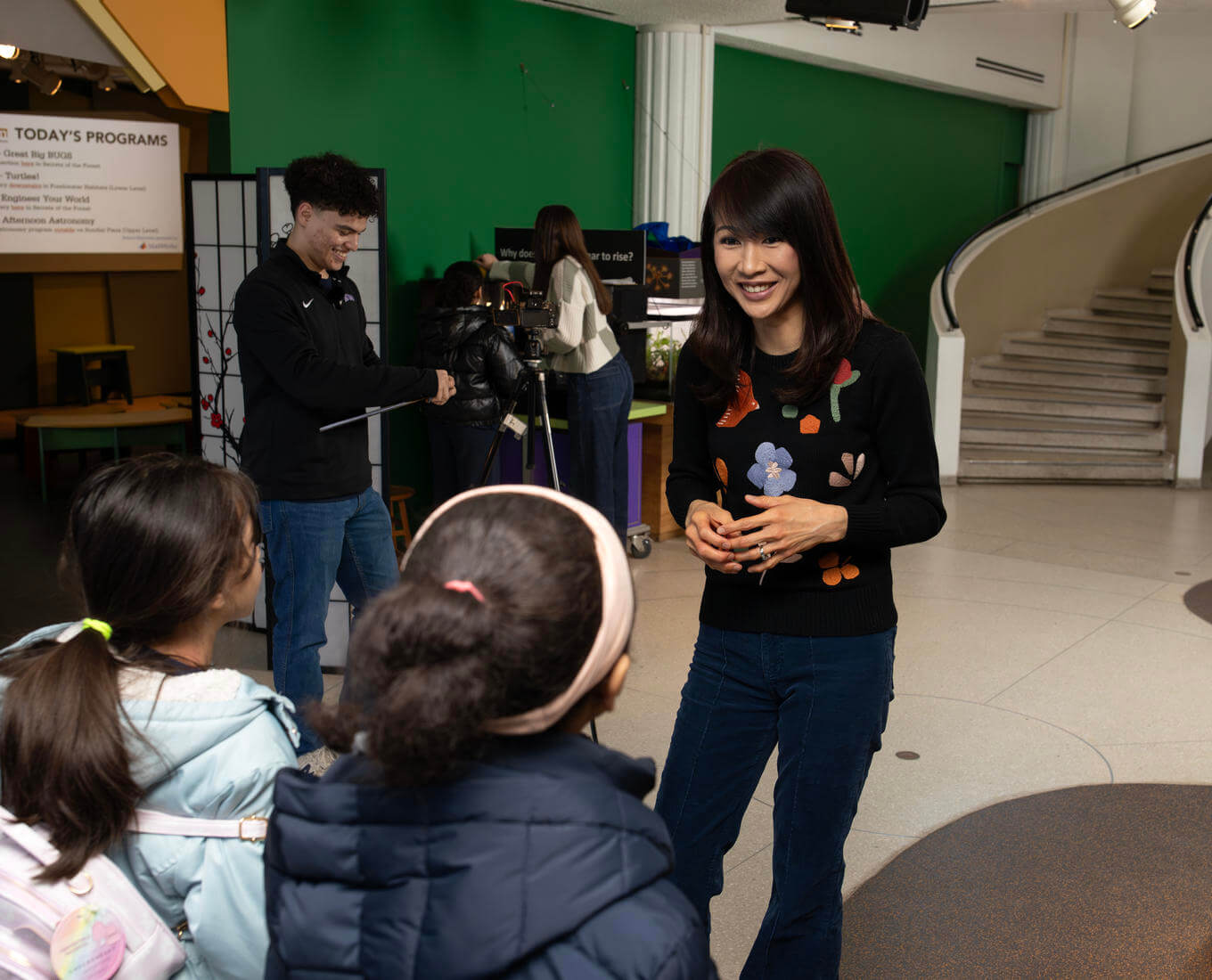 Woman speaks with children while setting up a science experiment at a museum.