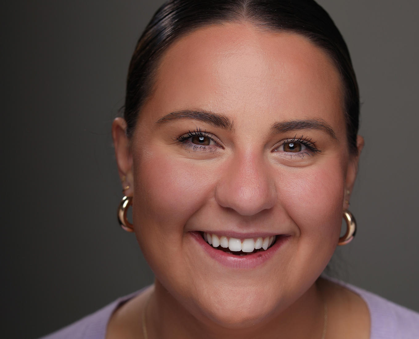 A portrait of a young woman with her hair tied back smiling 