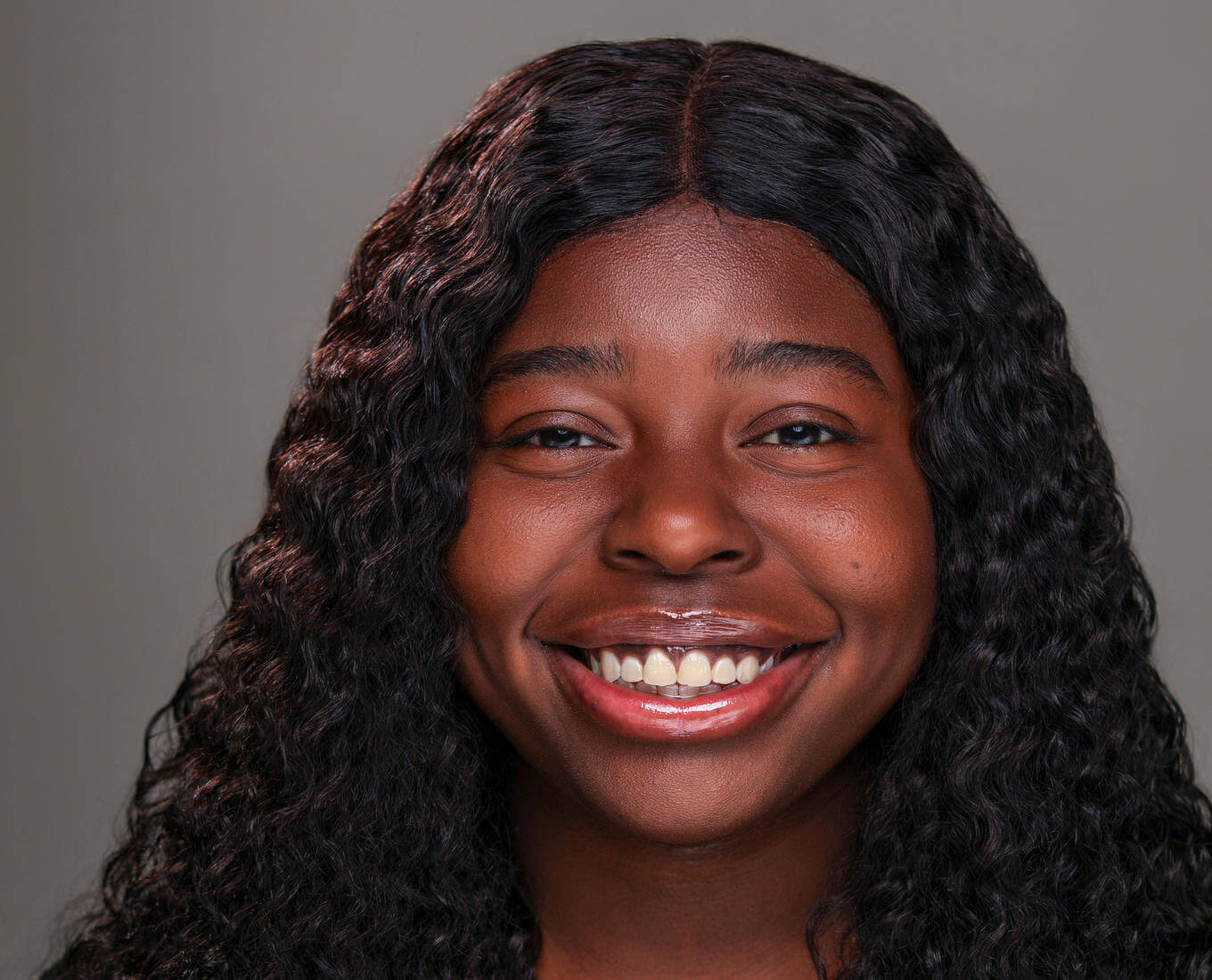 A portrait of a young woman with hair down to her shoulders and a collared shirt smiling