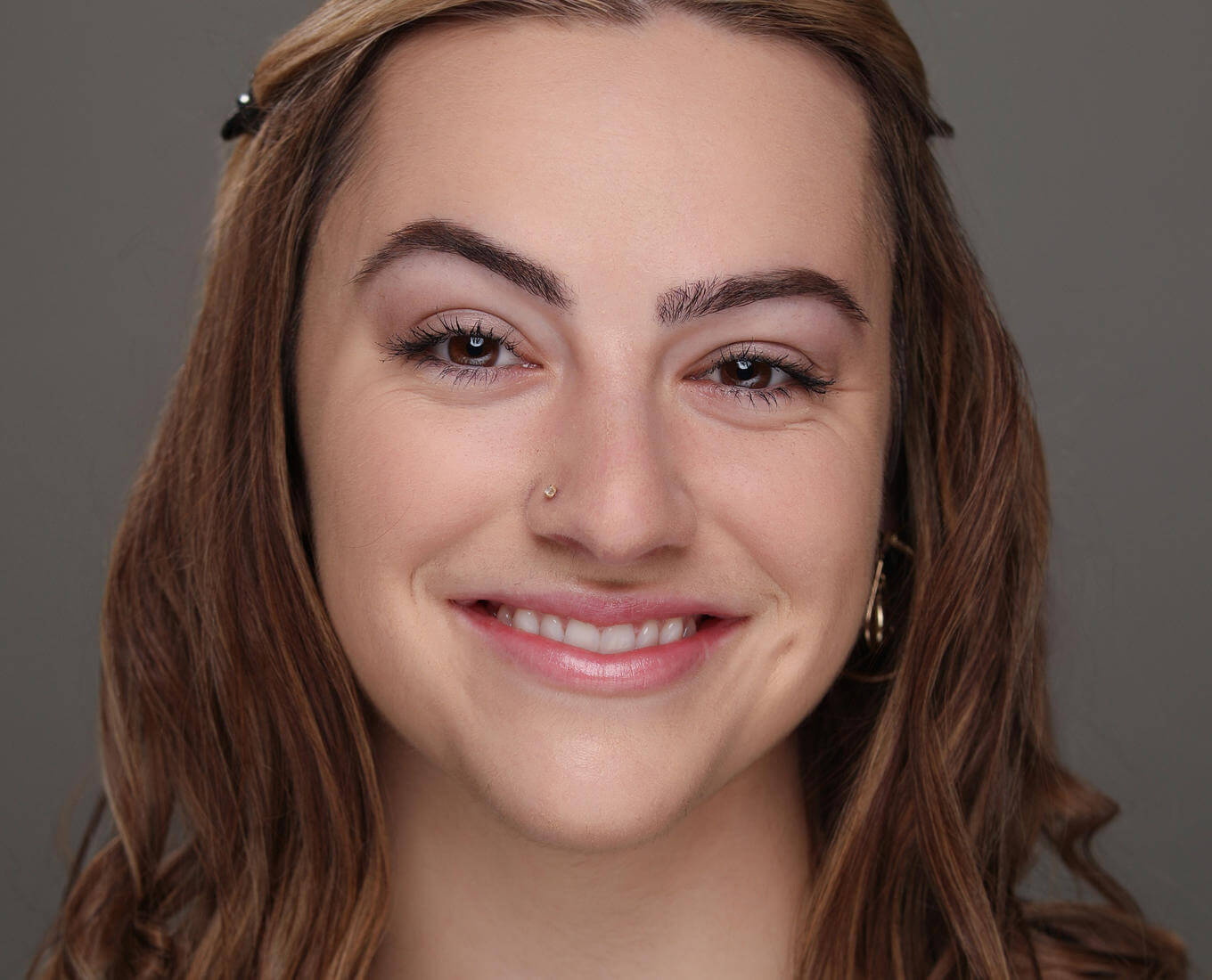 A portrait of a smiling young woman with wavy hair and wearing a gold pendant