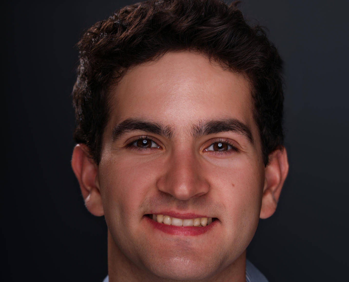 A portrait of a young man smiling with short hair and a collared shirt