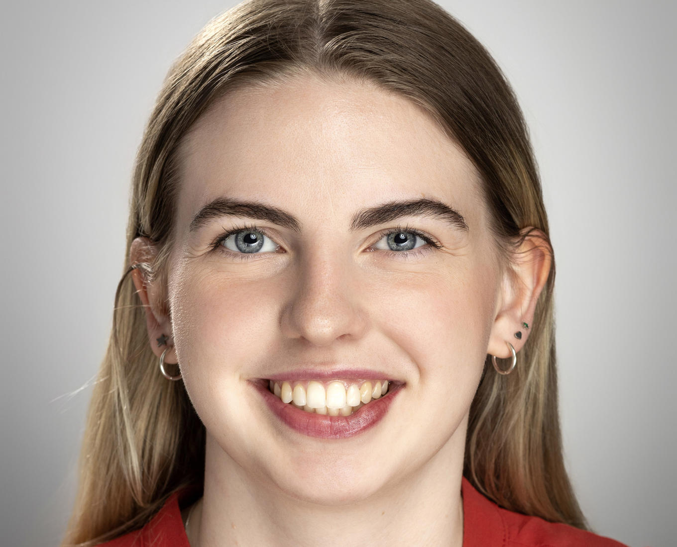 A young smiling young women in a red blouse with her hair pulled back behind her neck