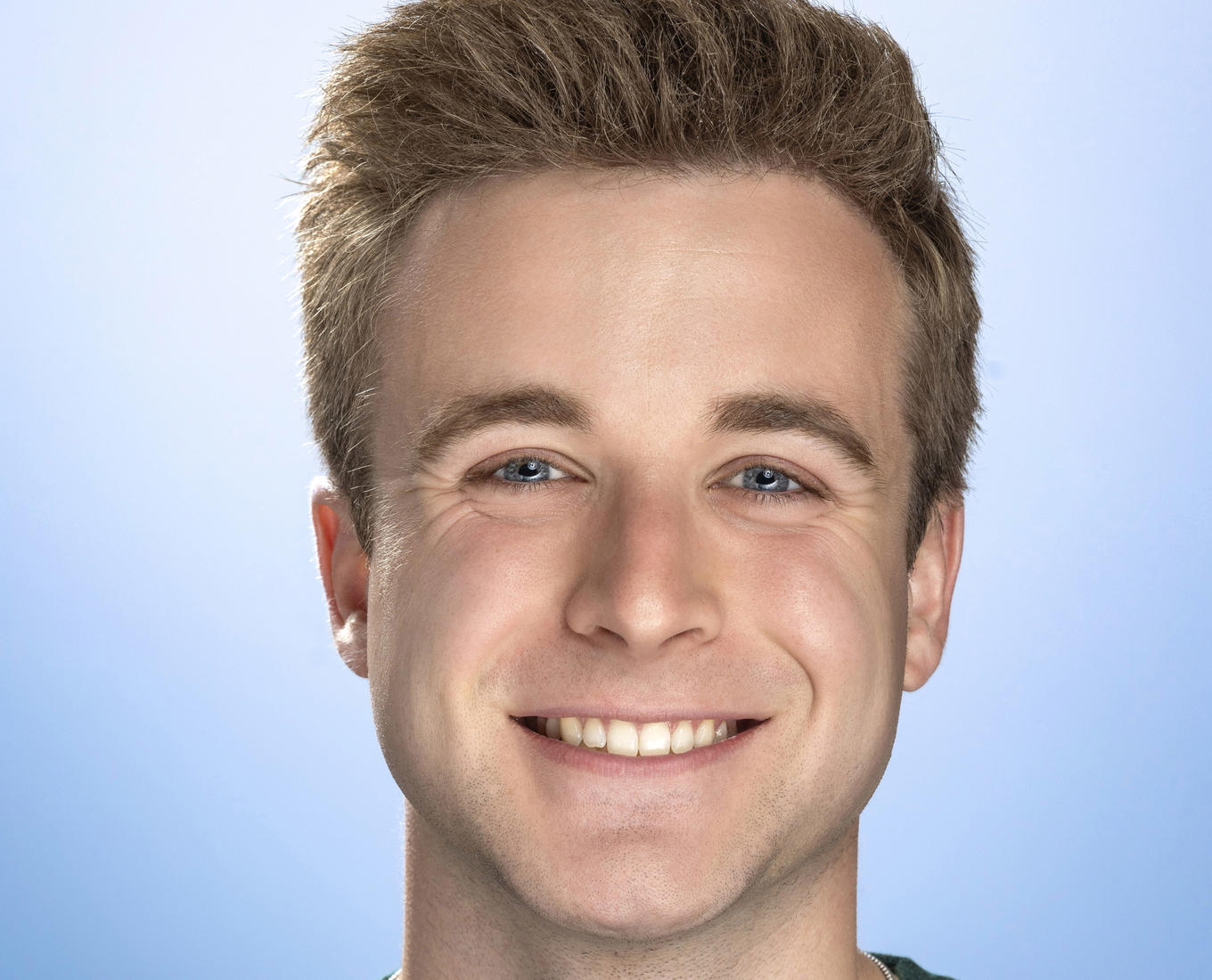 A smiling young man with wearing a green crew neck shirt and a necklace with a cross