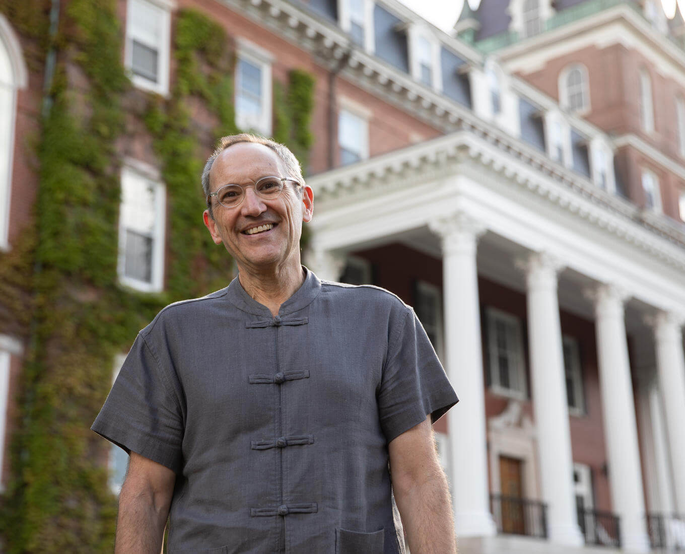 Professor stands in front of brick building with a white porch.