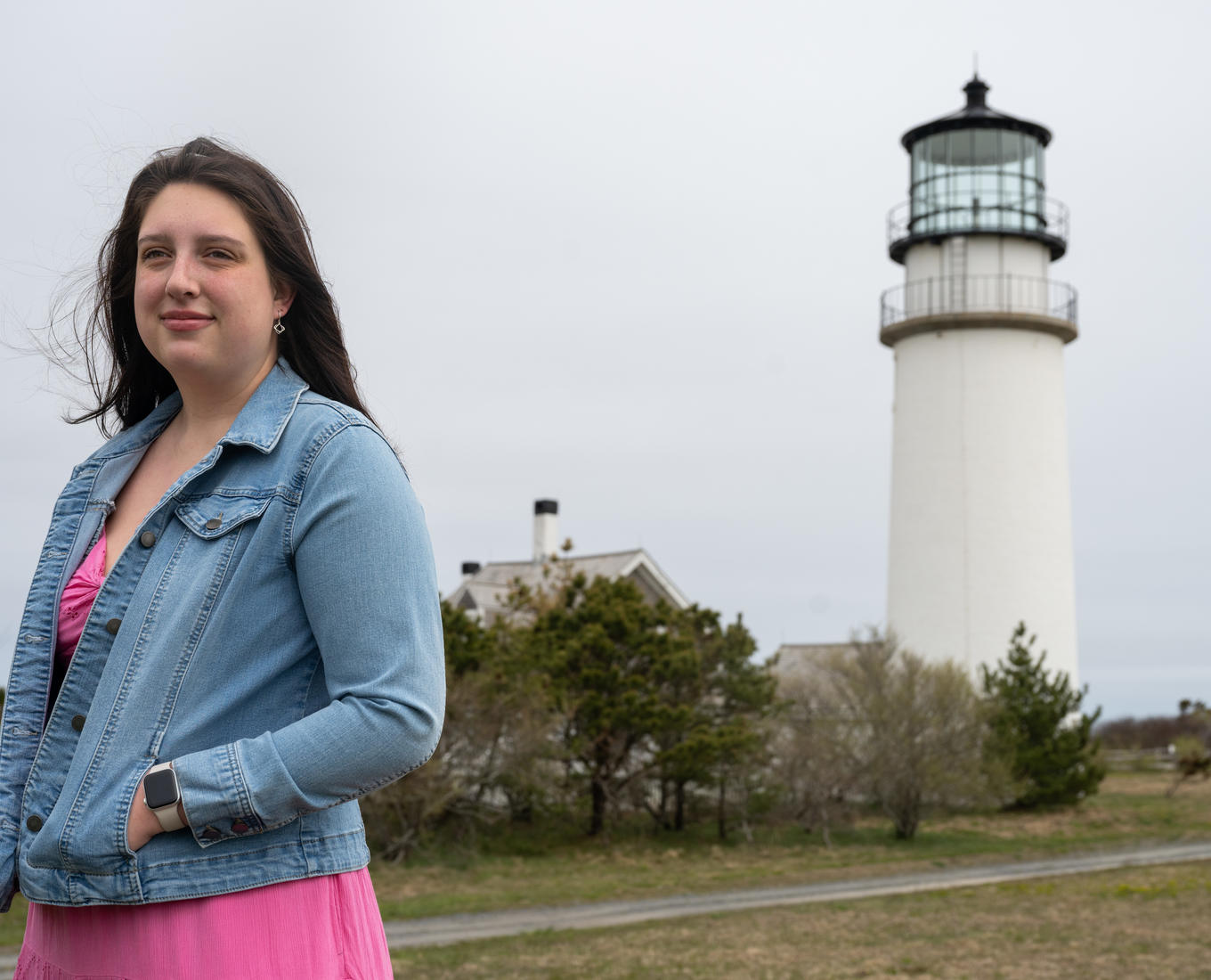 Young woman stands in front of a lighthouse on Cape Cod.