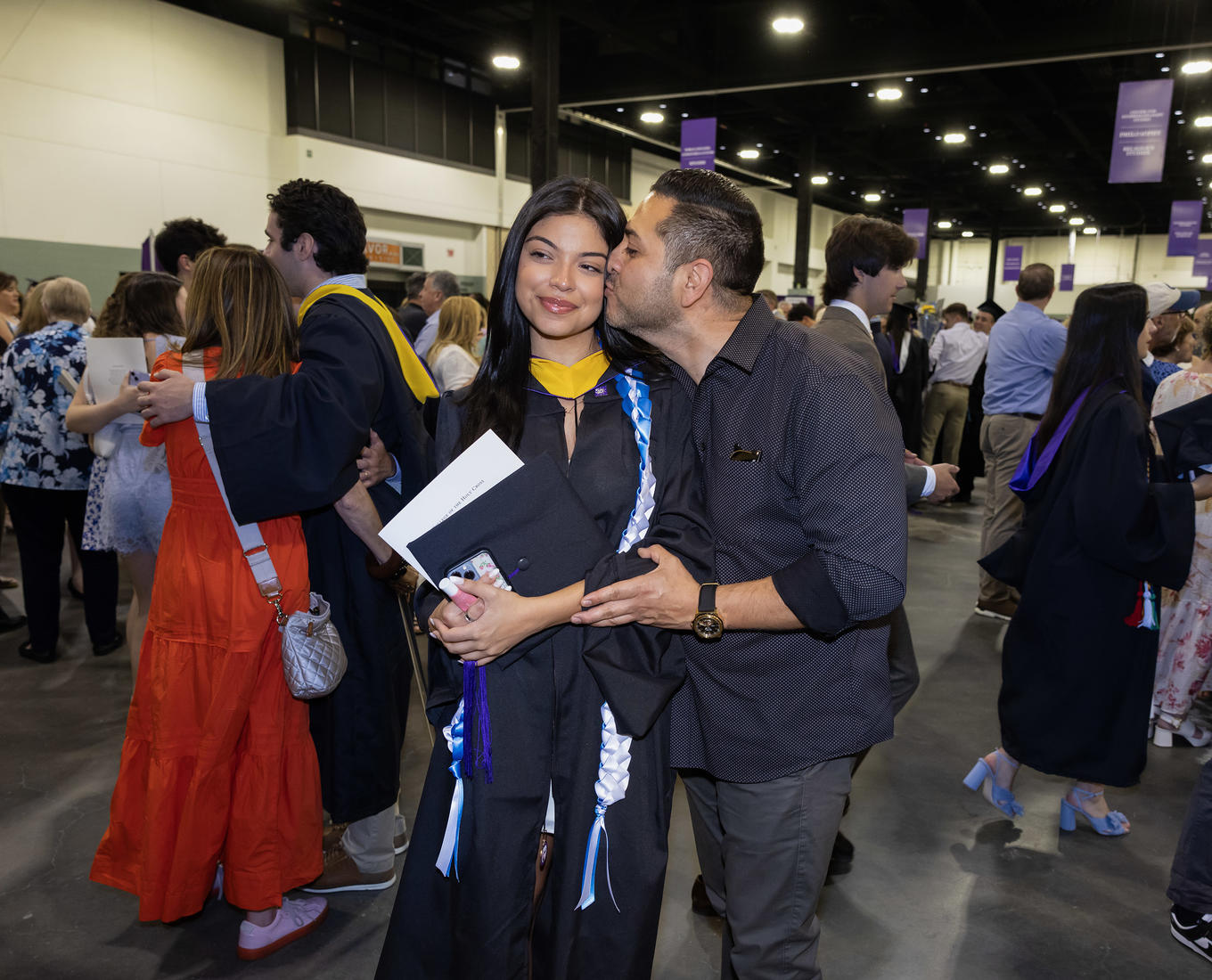 A dad kisses his daughter on the cheek after her graduation