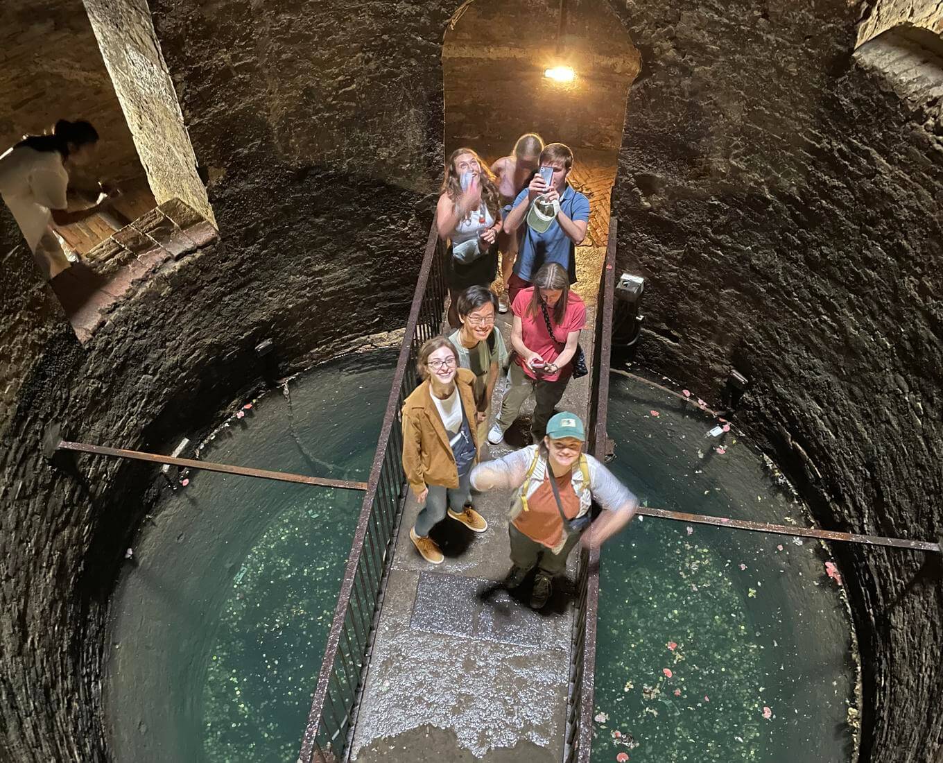 People stand on a bridge extending across the bottom of a giant well.