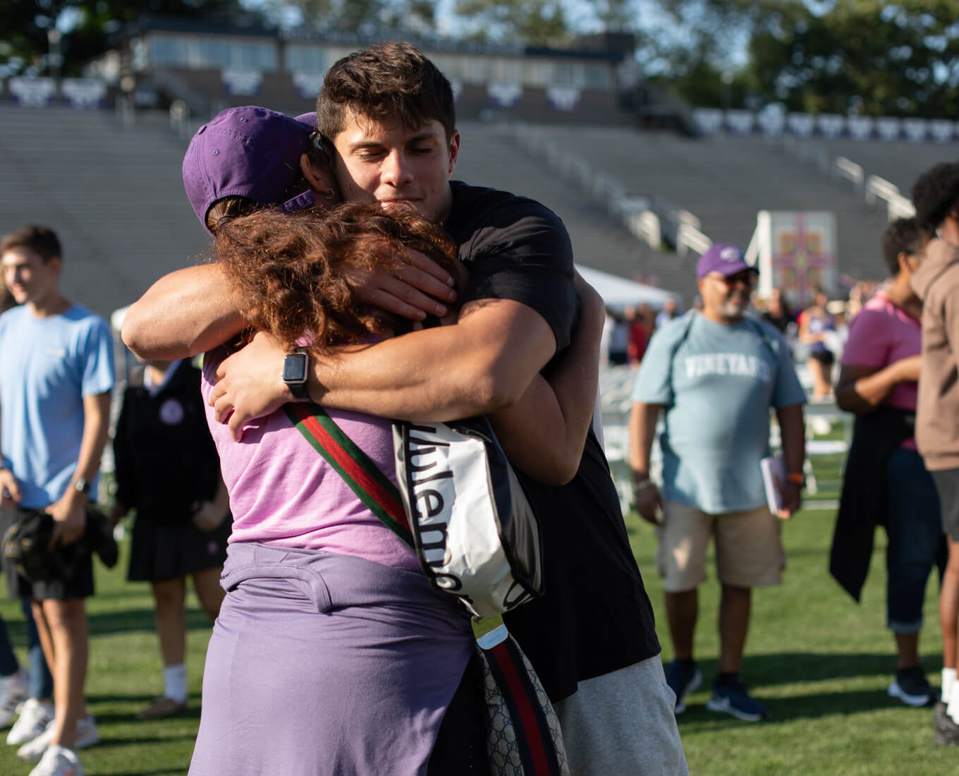 Mother and son embrace surrounded by others on a football field