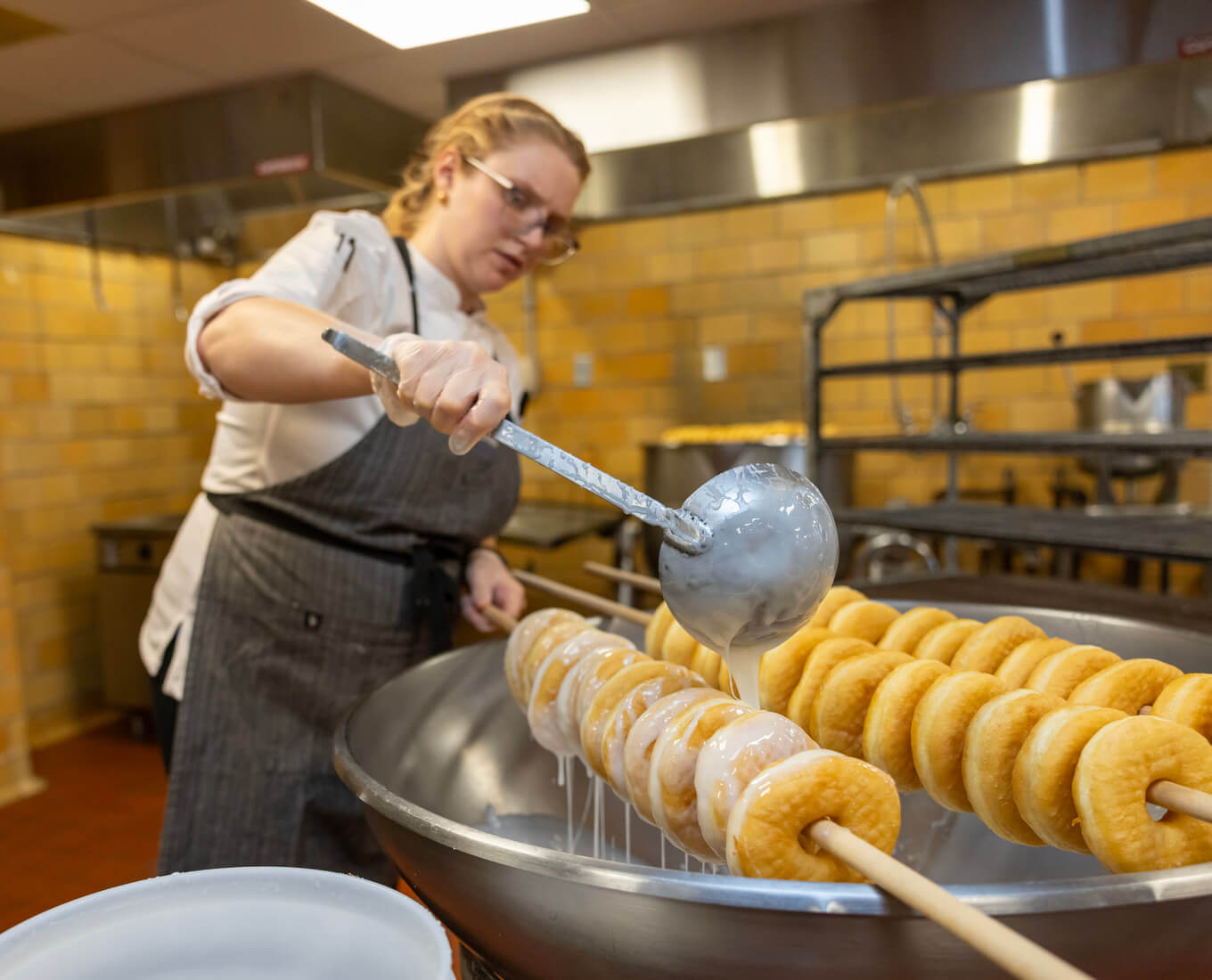 Woman ladles glaze over donuts