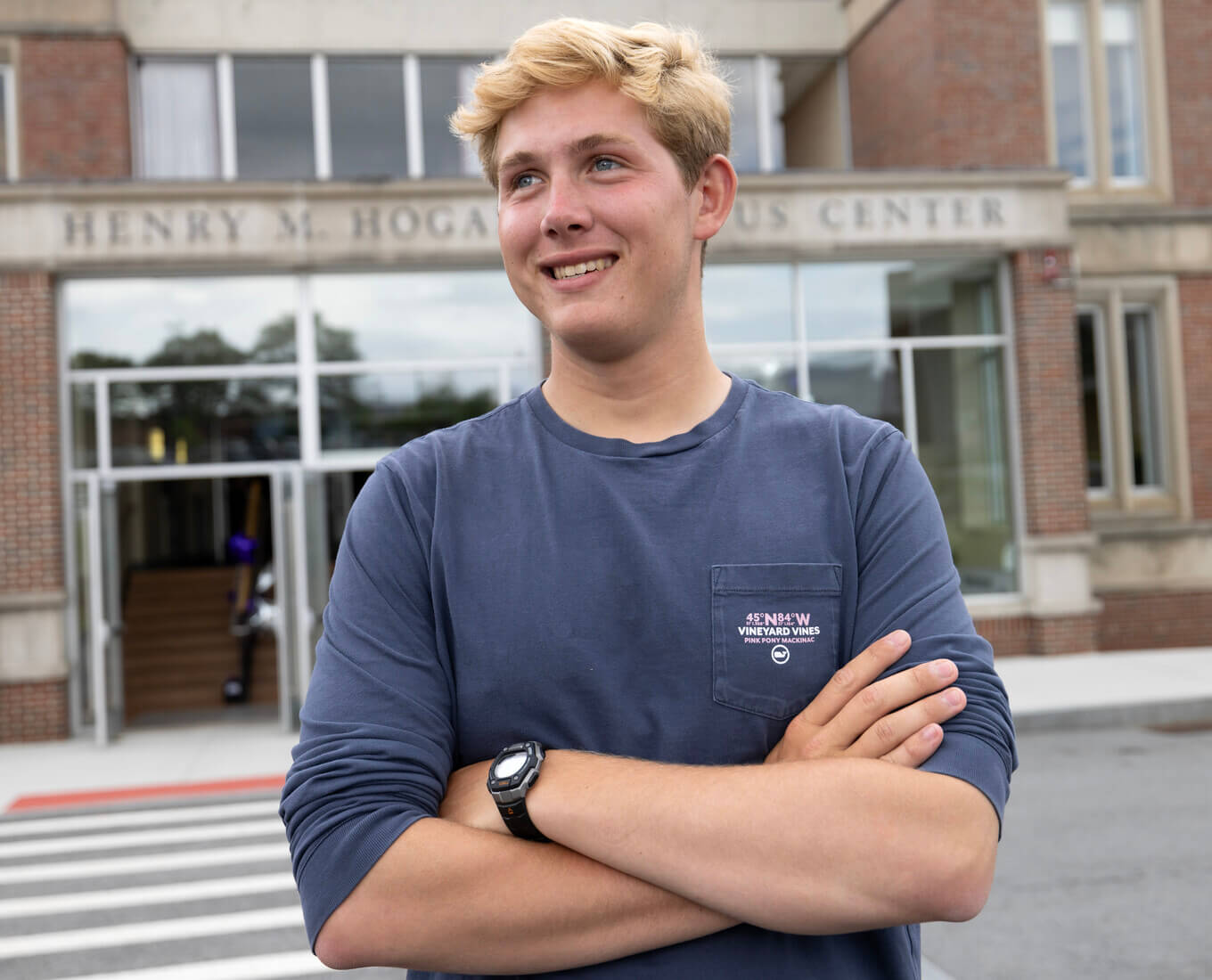 Blonde man standing in front of building with arms crossed.