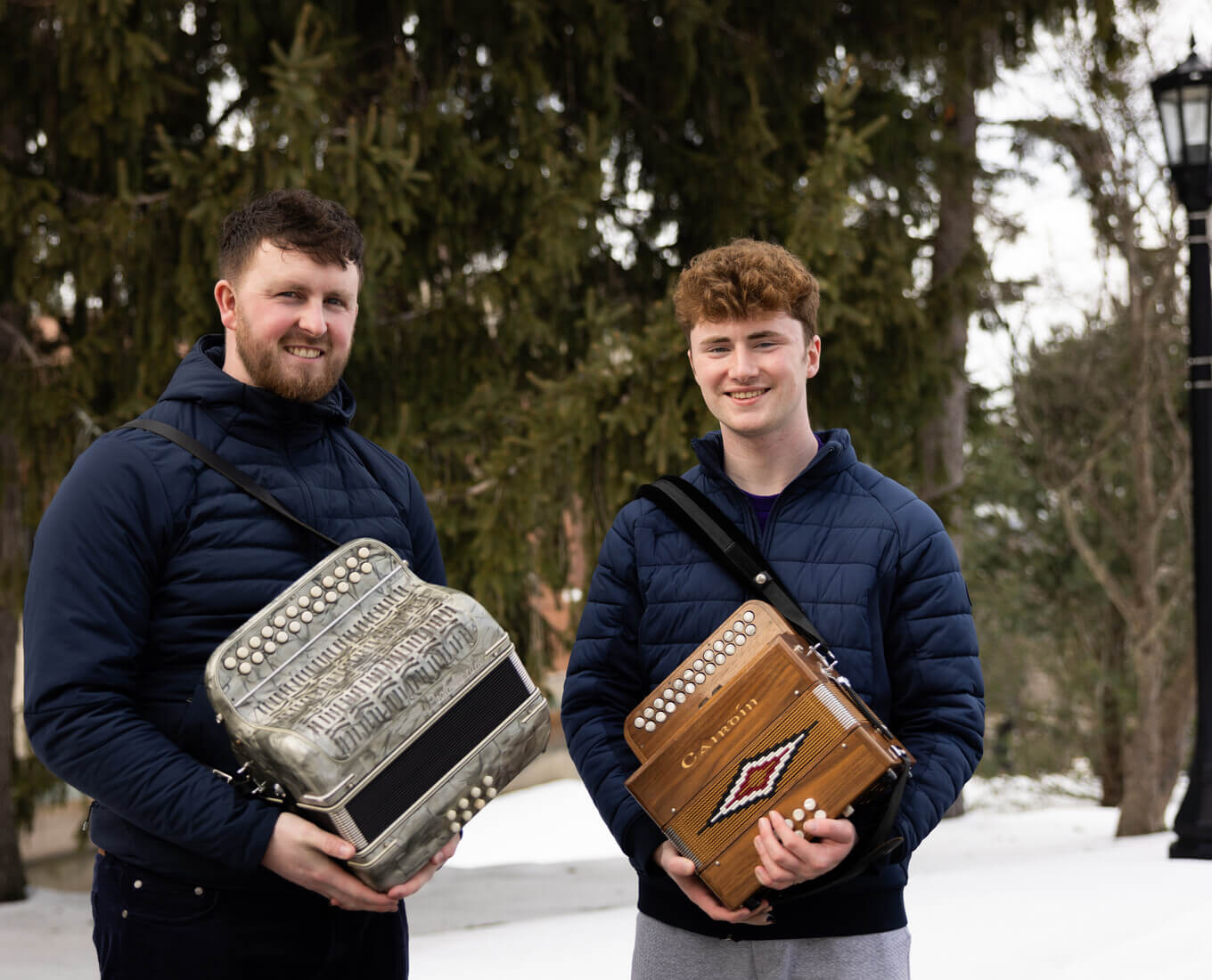 Two men holding button accordions in winter