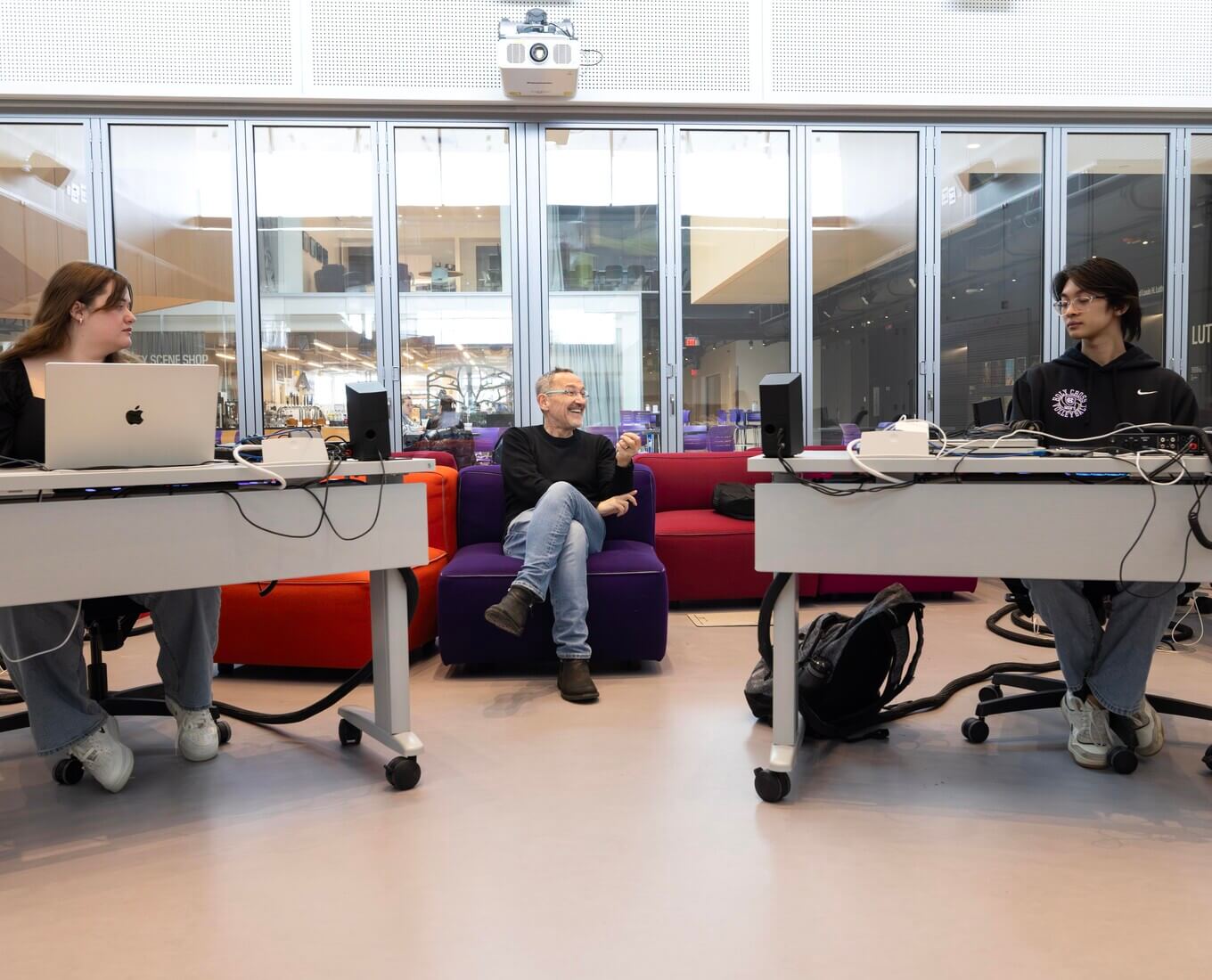 Man on couch in between two people at desks