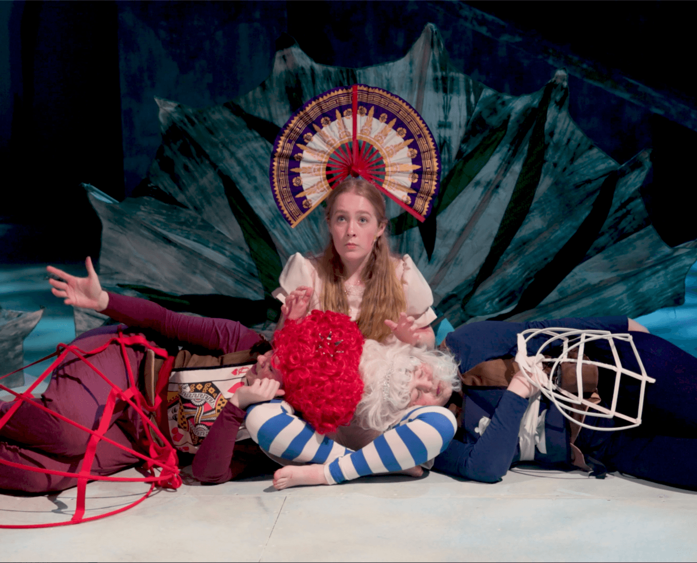 Blond woman sitting on stage, while two other people lay on the stage
