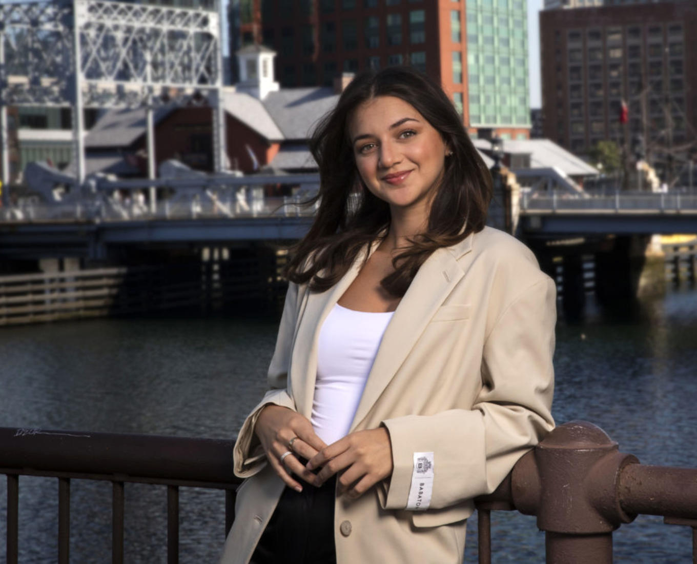 Woman leans against railing along a city harbor.
