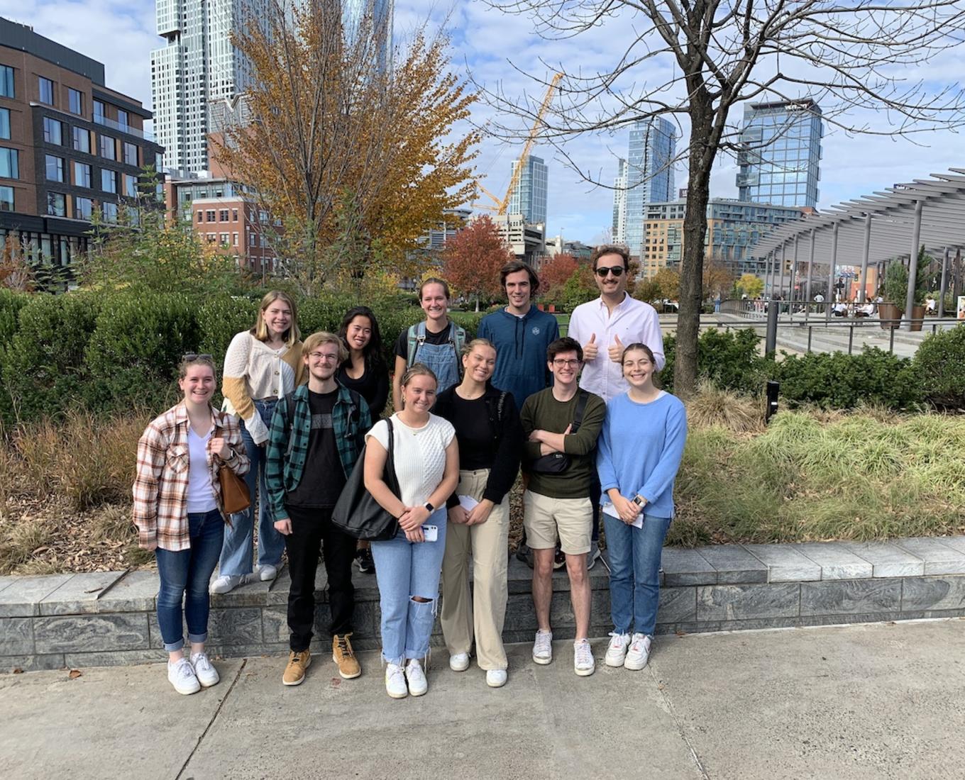 A group of men and women pose in a group in front of grennery.