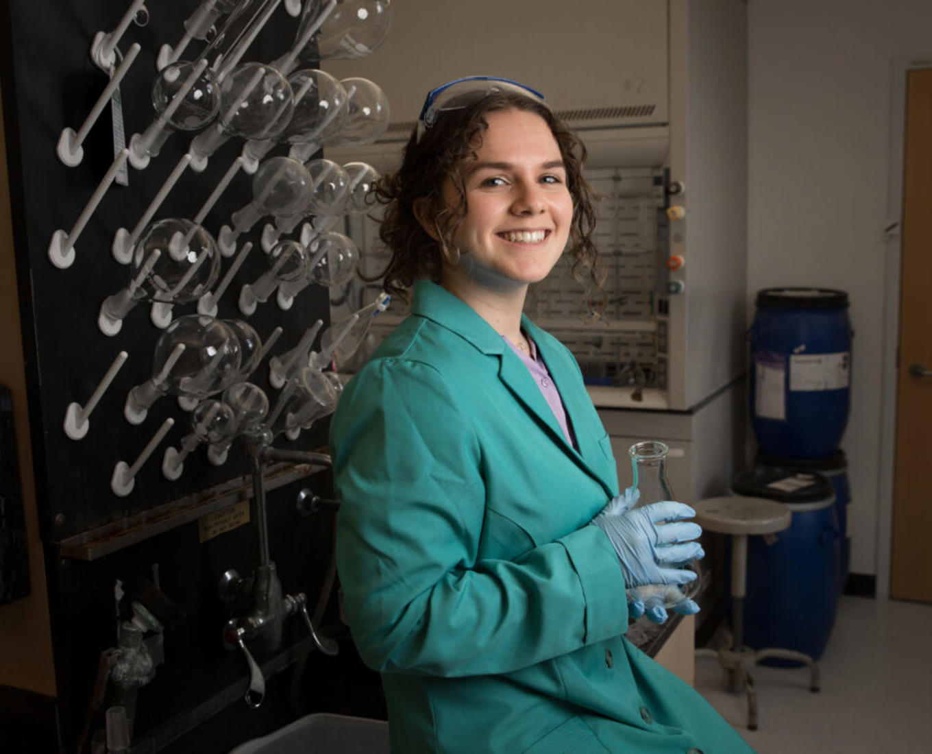 Young woman posing for picture in chemistry lab holding a glass beaker.