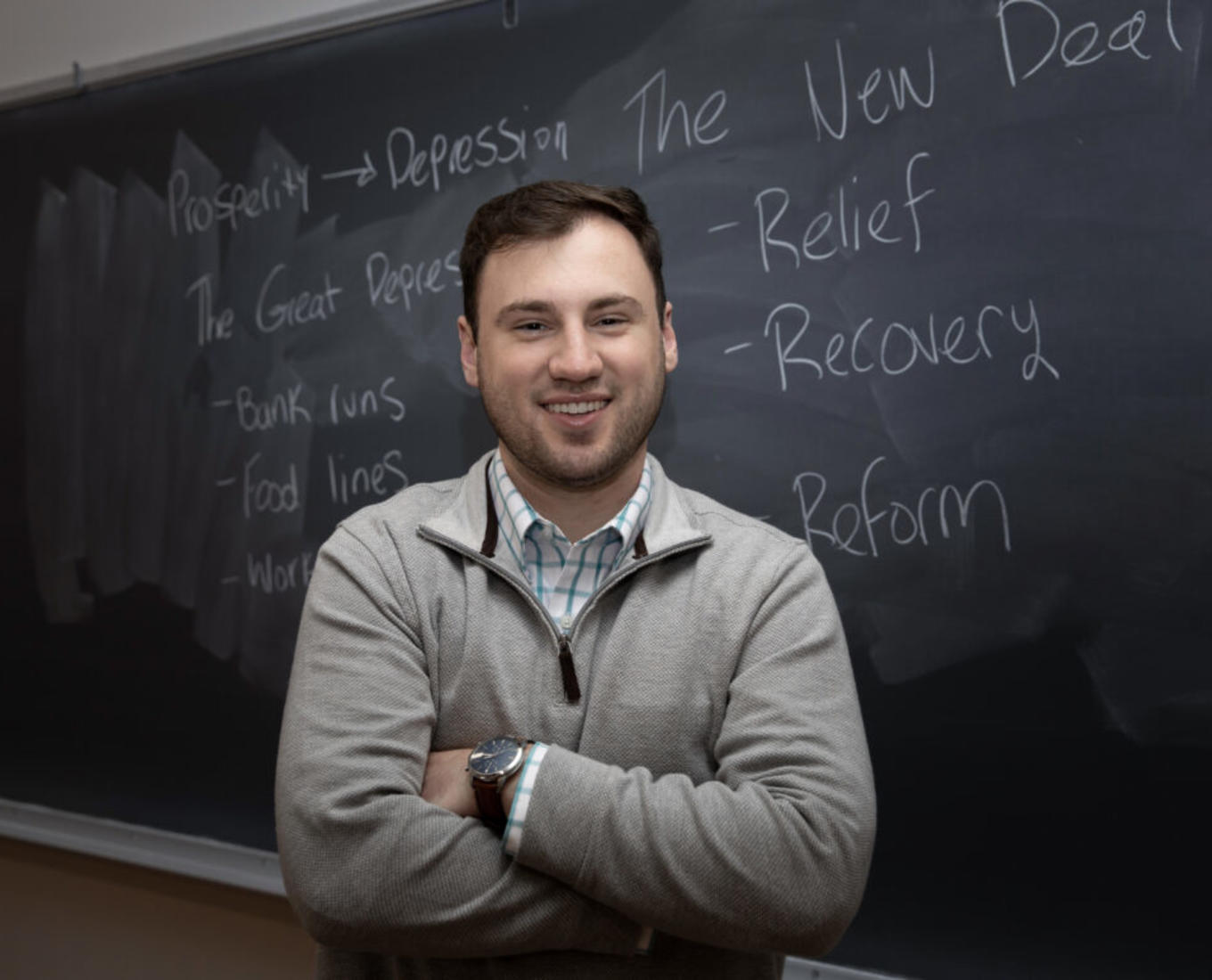 Male college student standing in front of a chalk board.