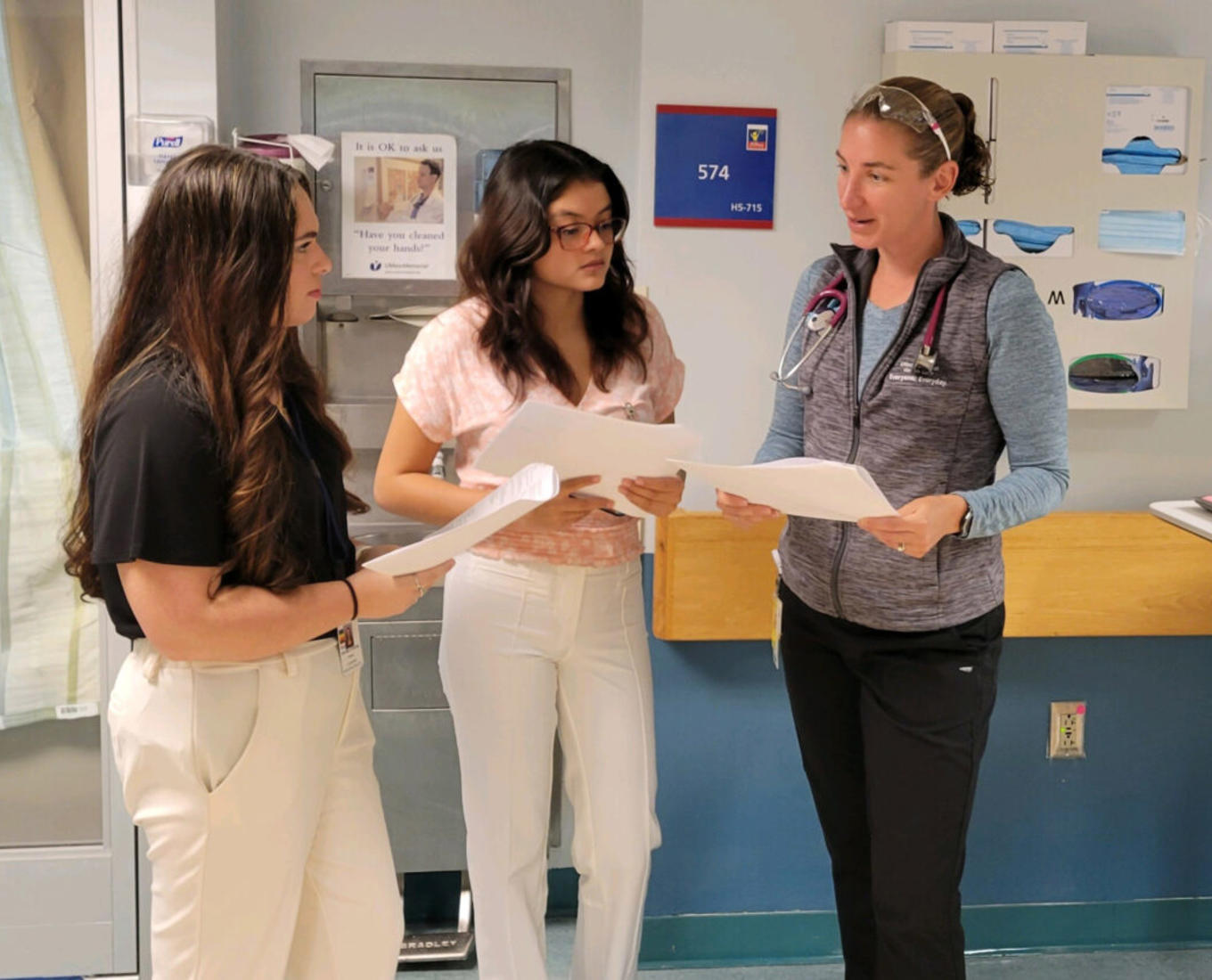 Three women discussing medical charts in clinical setting.