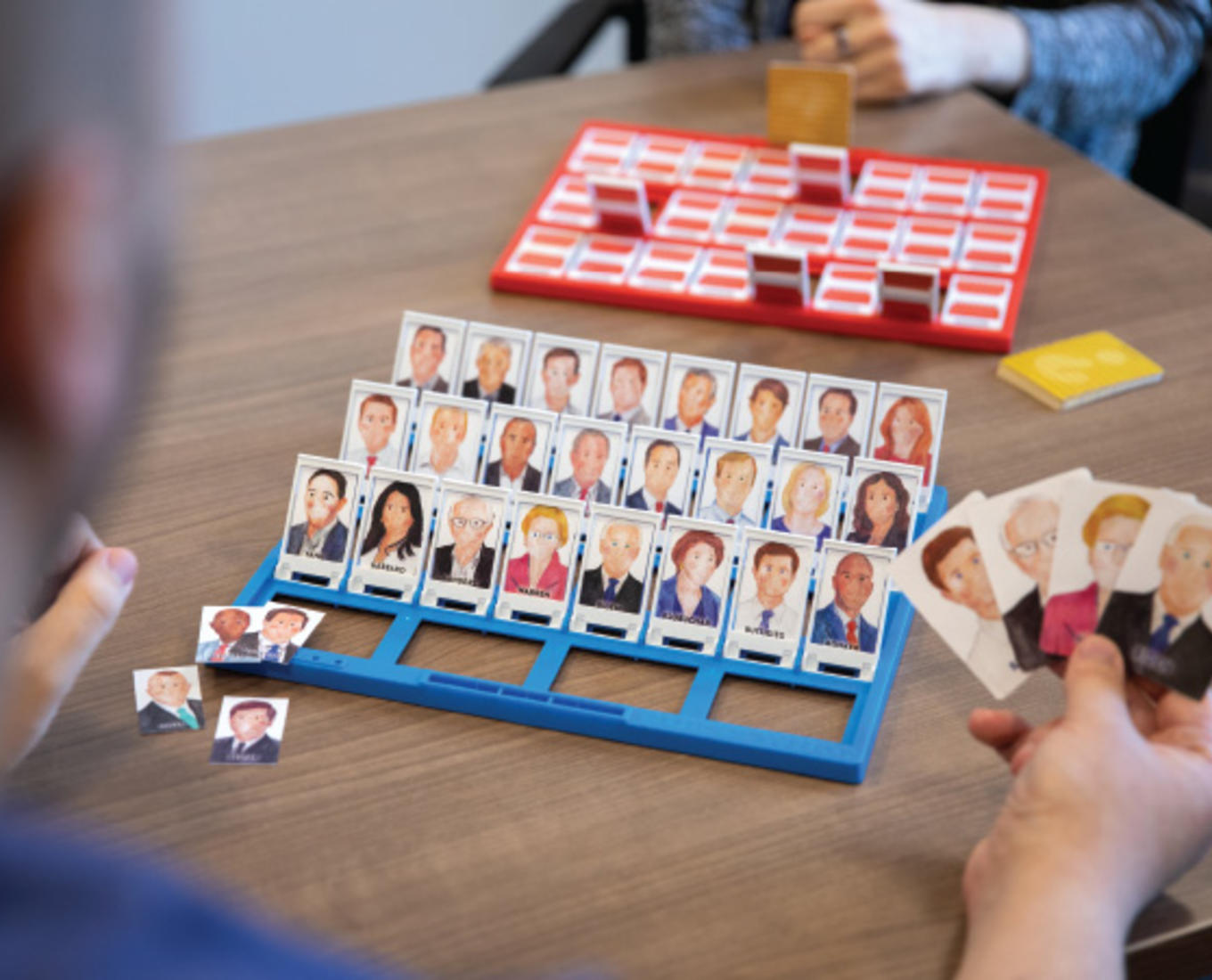 Two people play the game Guess Who where the faces have been switched for Democratic and Republican political figures