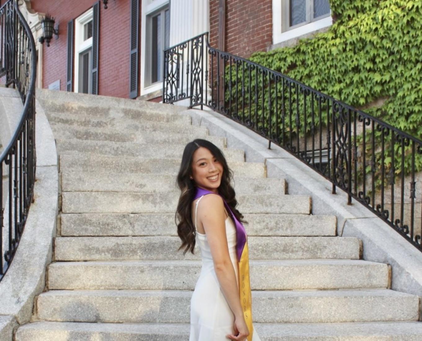 Isabelle Uong, a student at the College of the Holy Cross, poses at the base of granite stairs in a white dress.