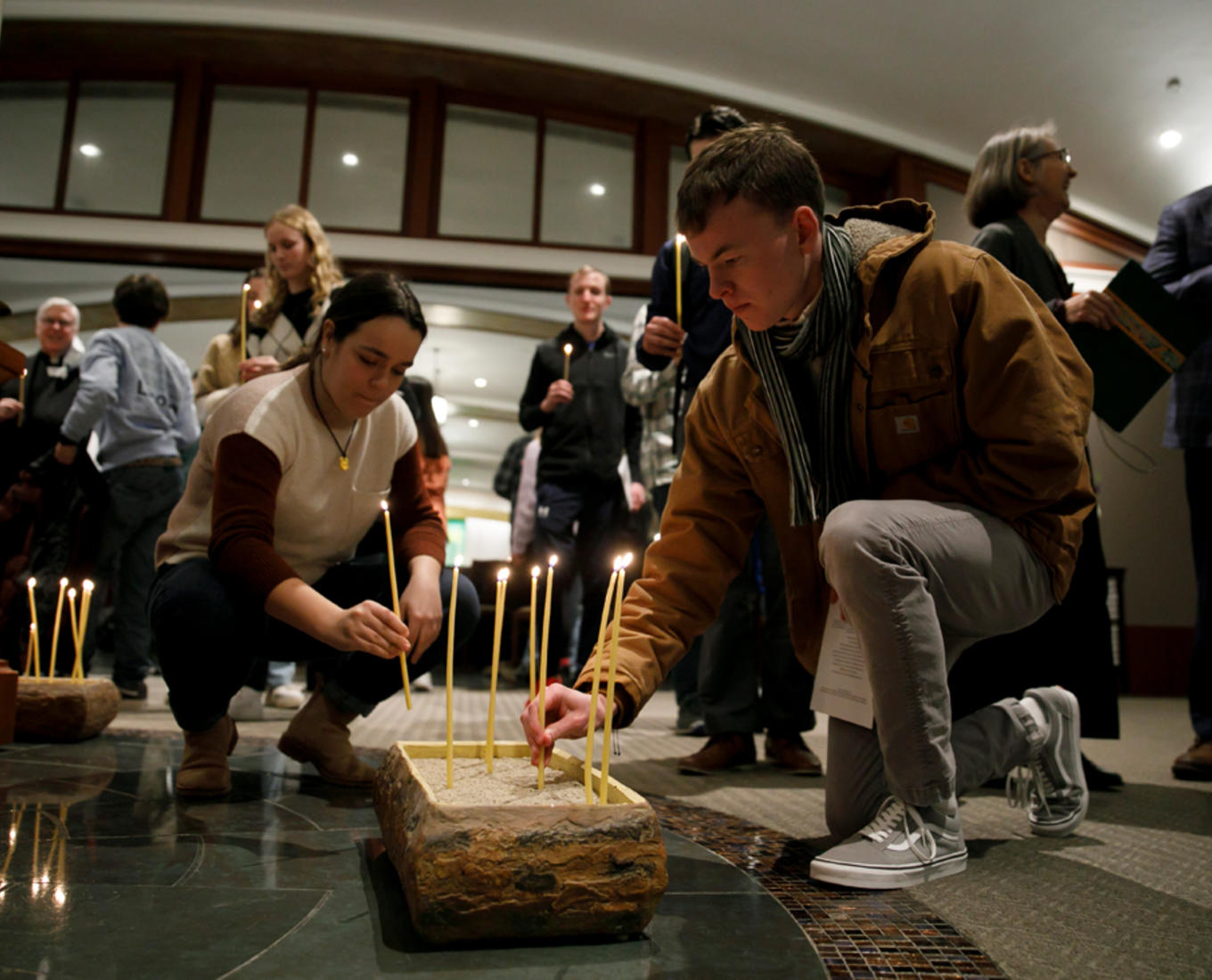 A man and a woman place lit candles in a holder
