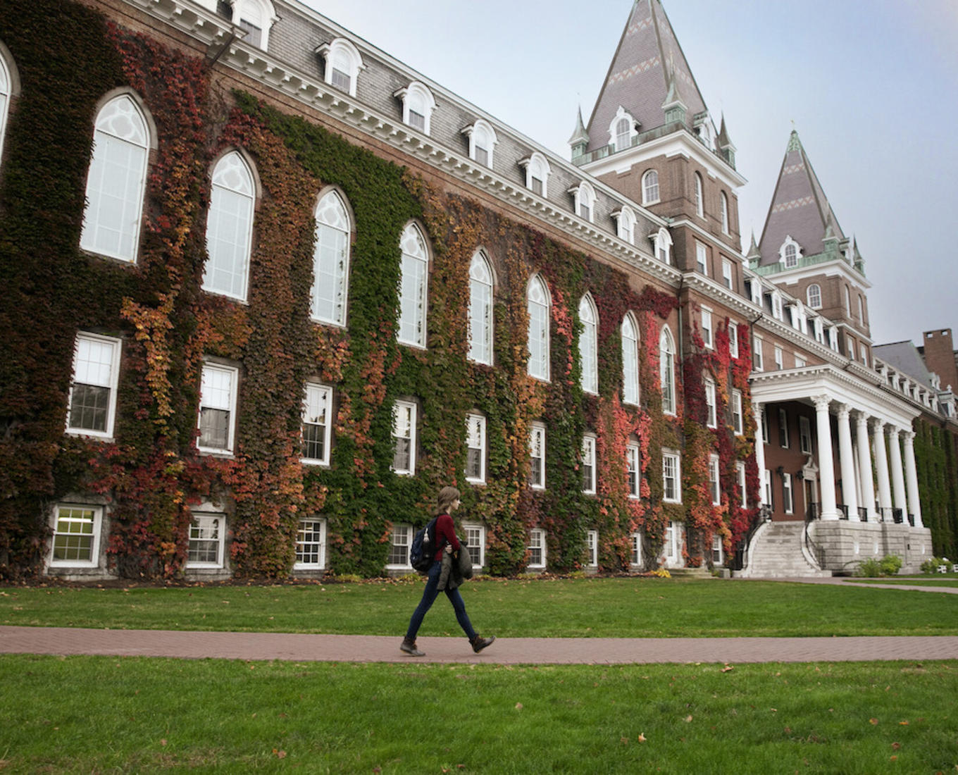 A person walks by an ivy-covered brick building.