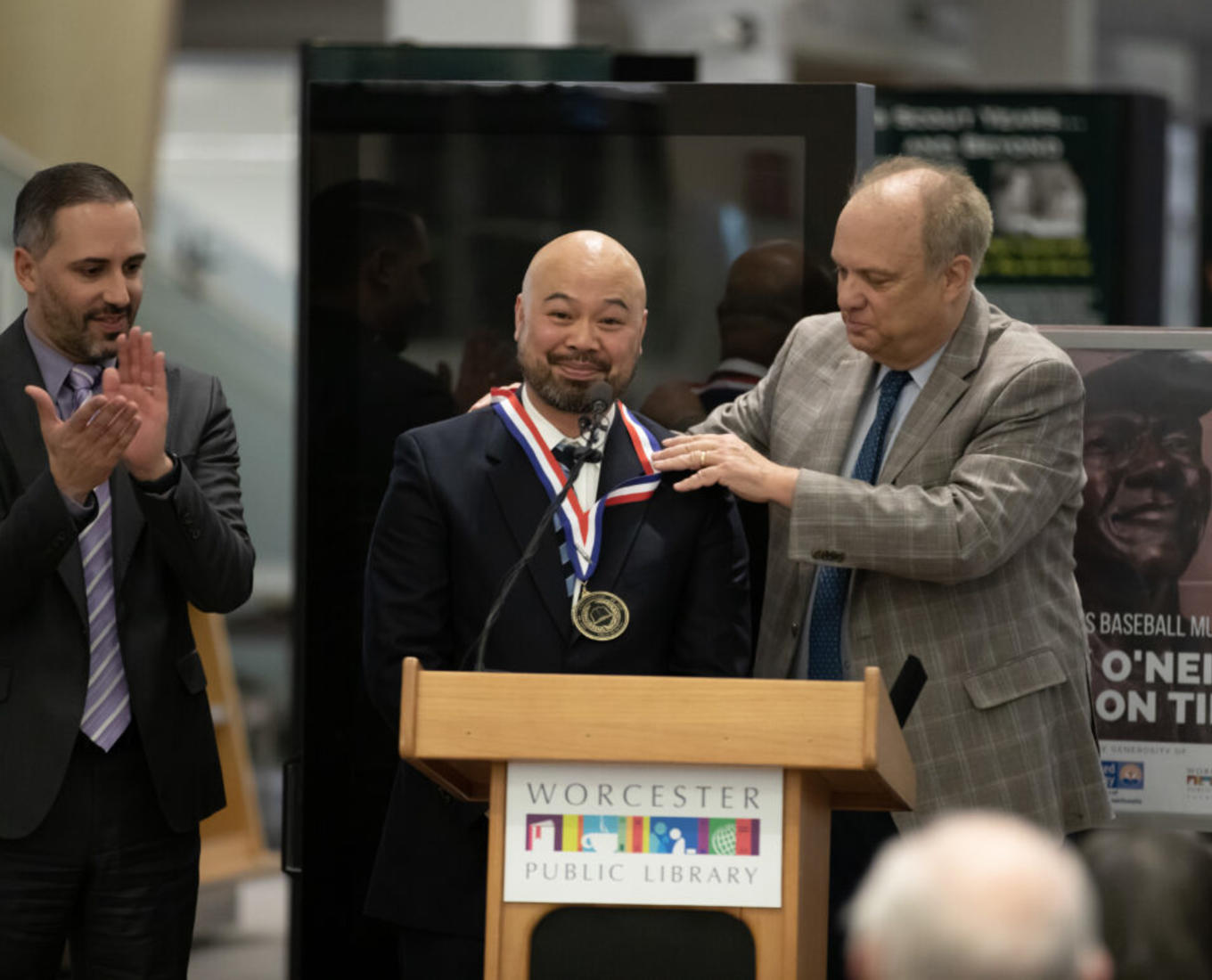 Man stands a podium with honorary medal around his neck