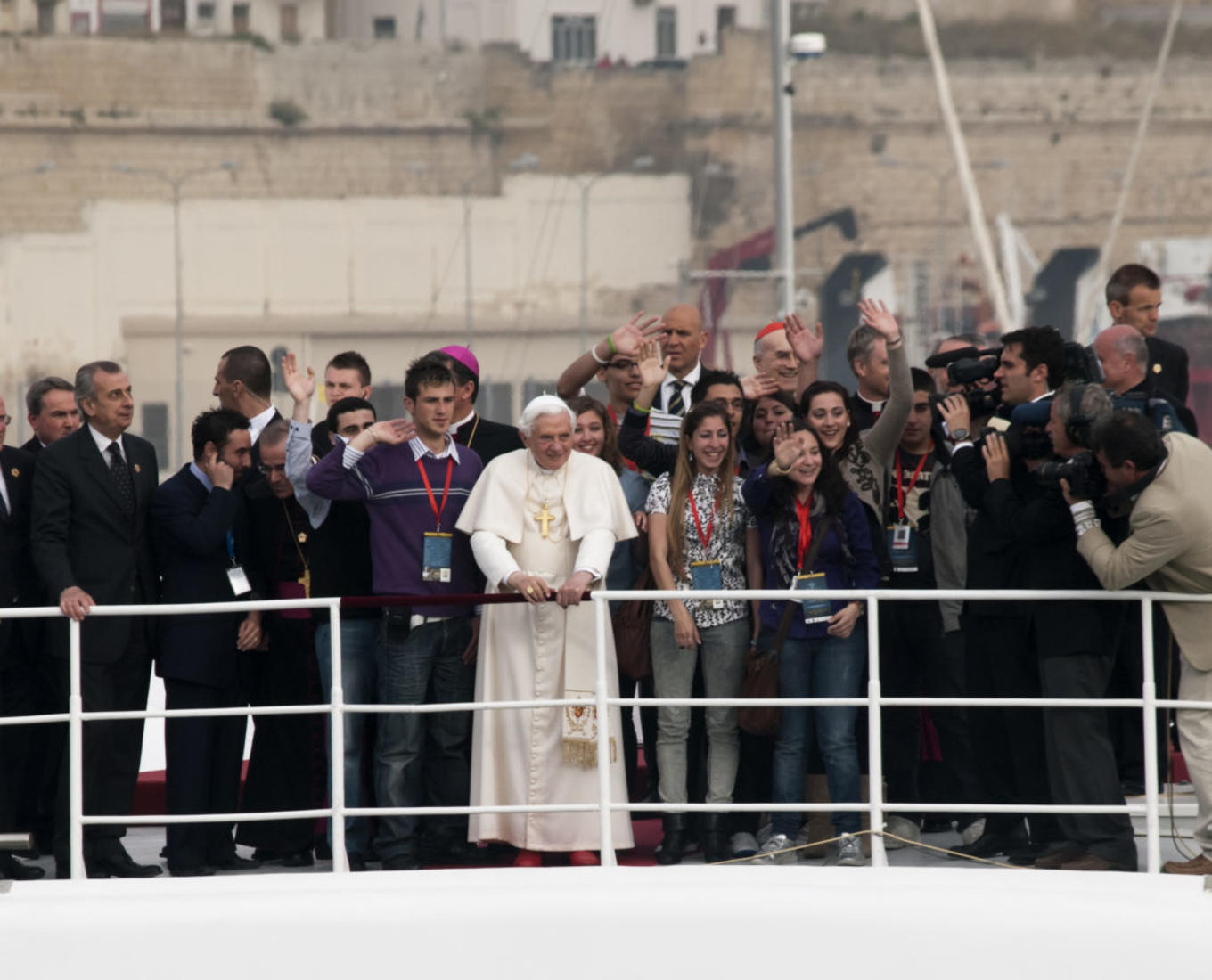 Pope Benedict XVI stands with a crowd on a dock.