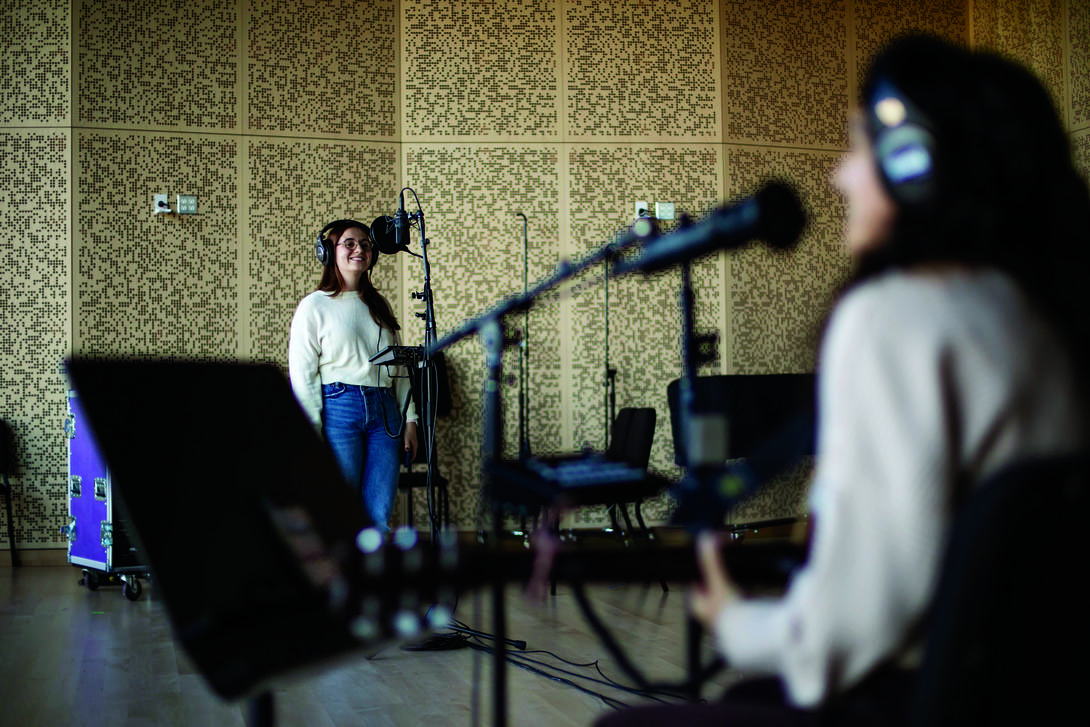 Two students practice vocals in front of a microphone.