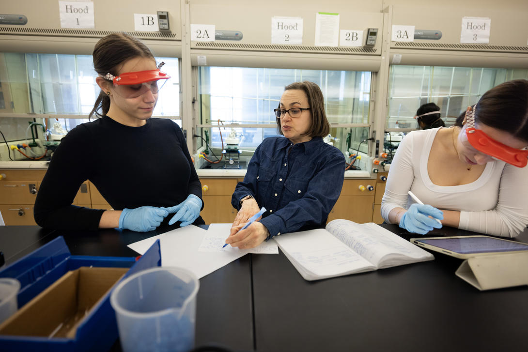 Two female students work with a female professor in a chemistry lab.