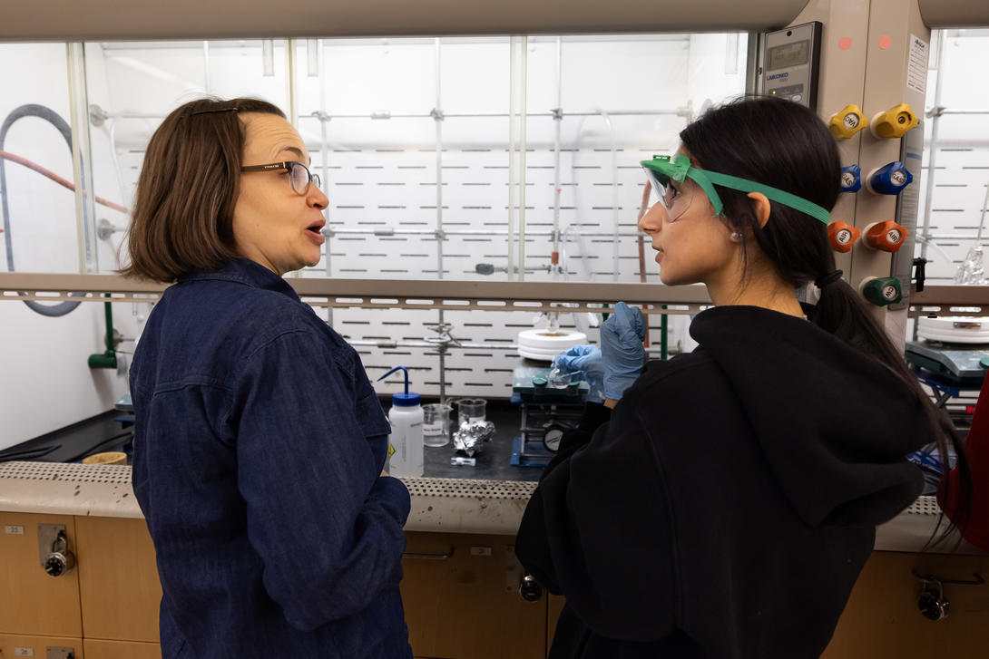 A female chemistry professor talks with a student in lab.