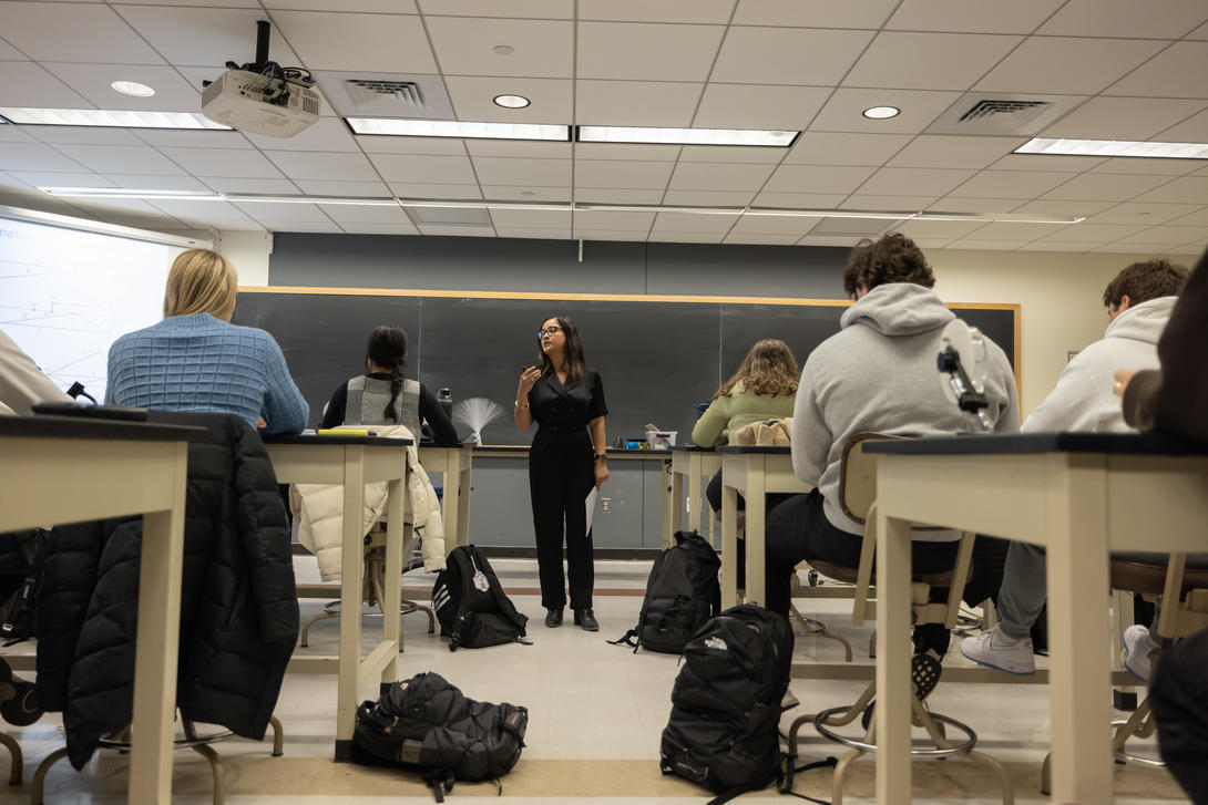 Female physics professor stands at front of classroom. 